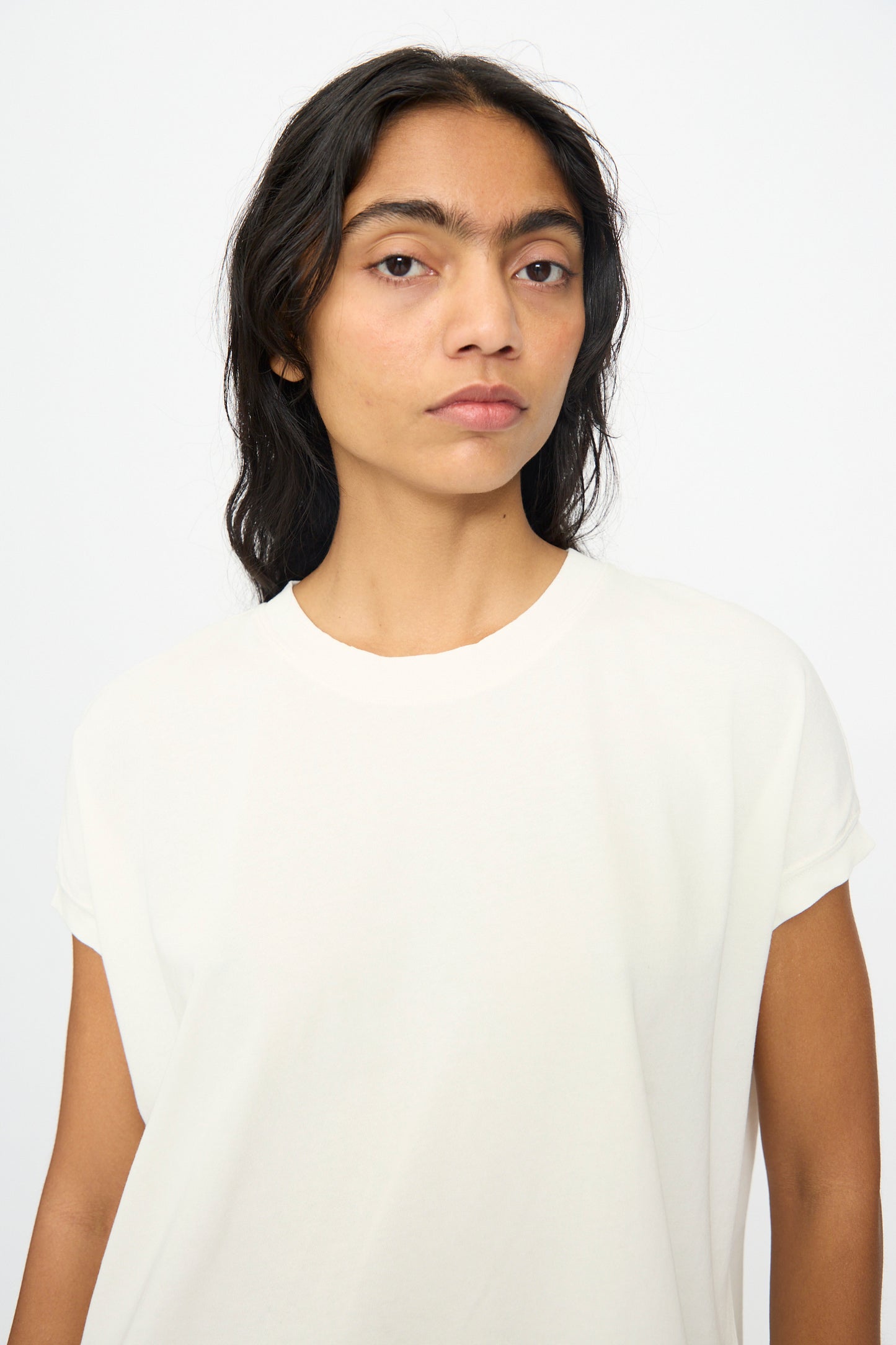 A person with long dark hair wears the Ichi Antiquités Cotton Sleeveless Tee in White, made in Japan, standing against a light background and looking directly at the camera with a neutral expression.