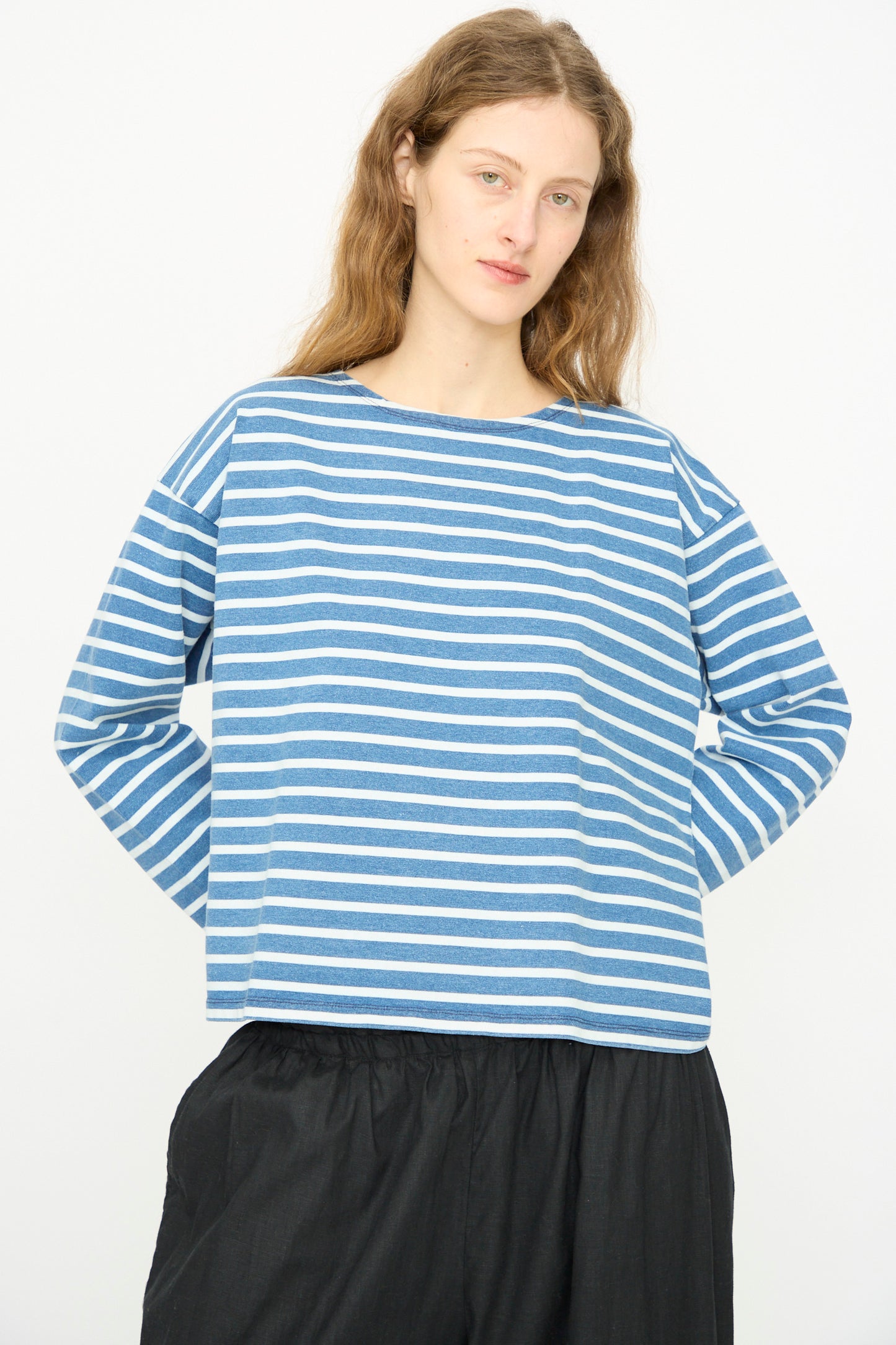 A person with long light brown hair models the Ichi Antiquités Cotton Stripe Pullover in Blue and White with black pants, standing against a plain white background.