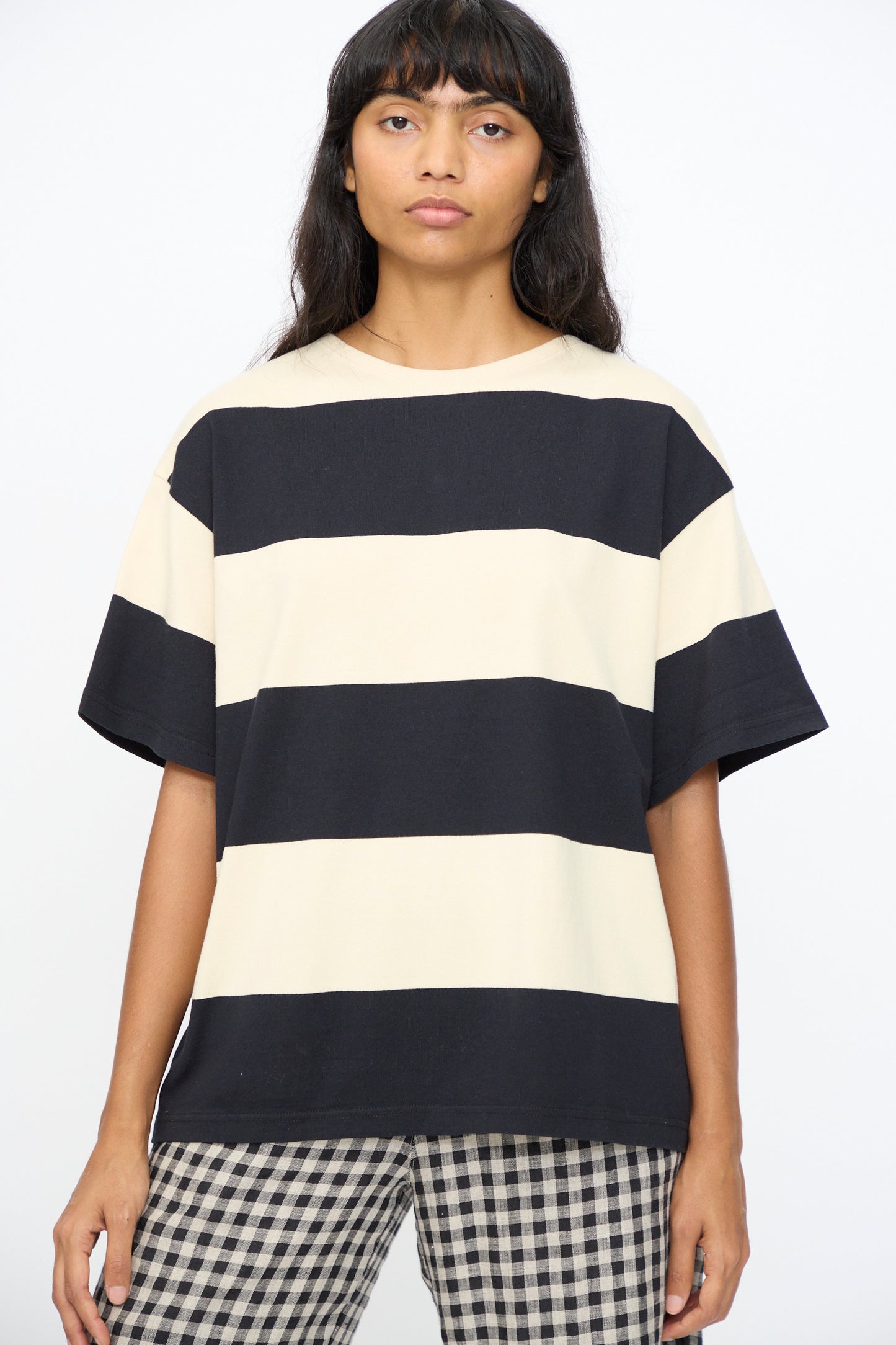 A person wearing the Ichi Antiquités Cotton Stripe Pullover in Natural and Black, made in Japan, paired with checkered pants, stands against a plain background.