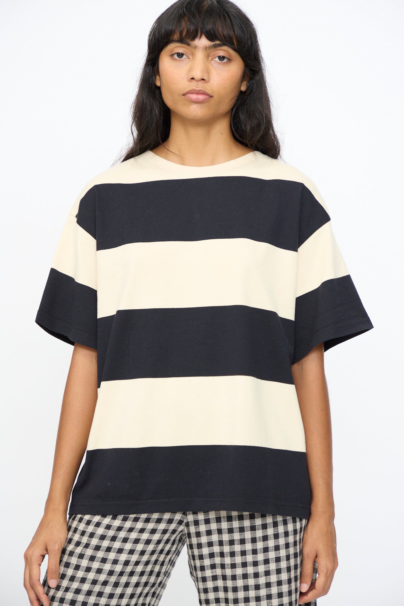 A person wearing the Ichi Antiquités Cotton Stripe Pullover in Natural and Black, made in Japan, paired with checkered pants, stands against a plain background.