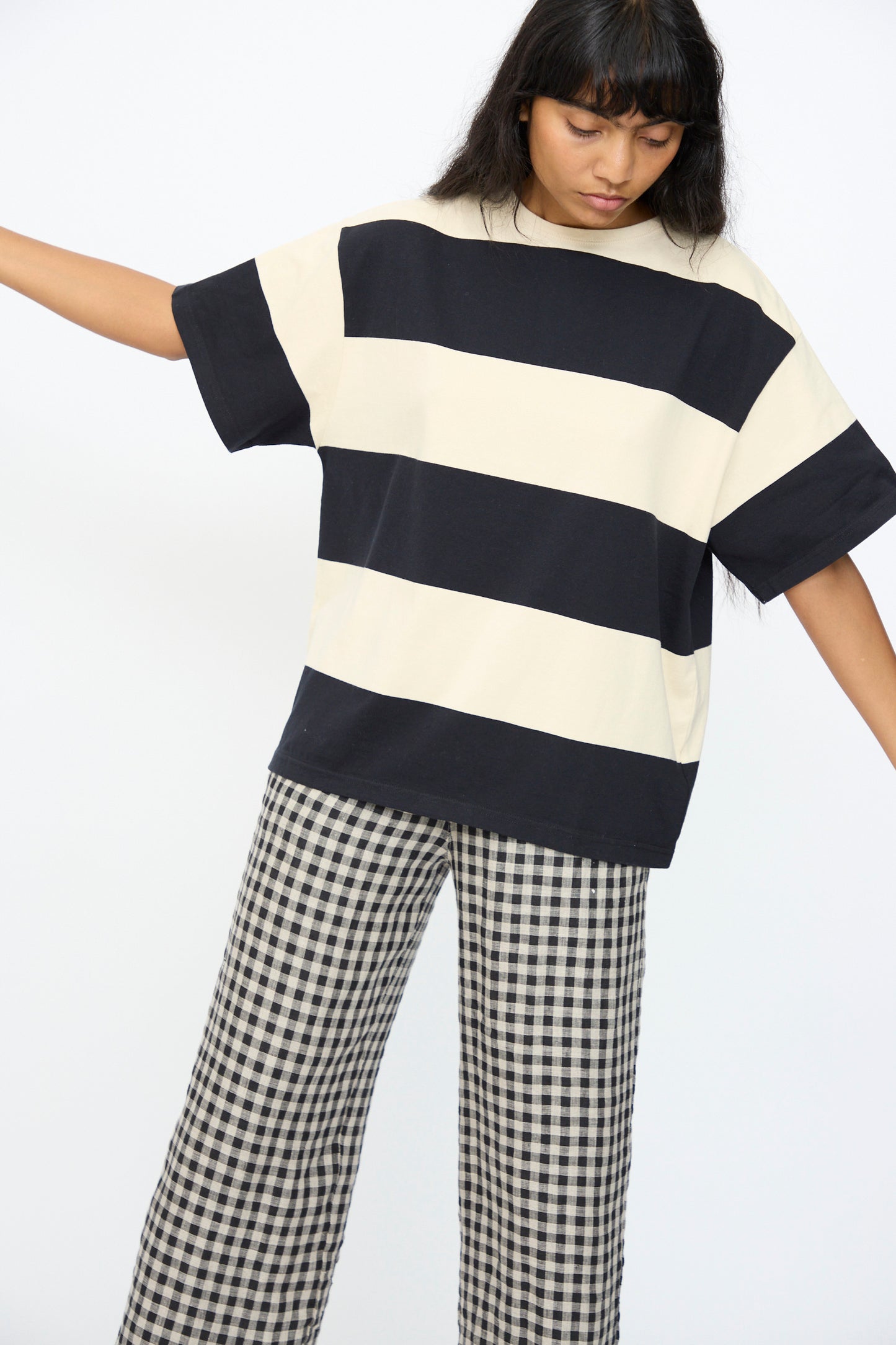 A person wears the Ichi Antiquités Cotton Stripe Pullover in Natural and Black, paired with black and white checkered pants, standing against a plain white background.