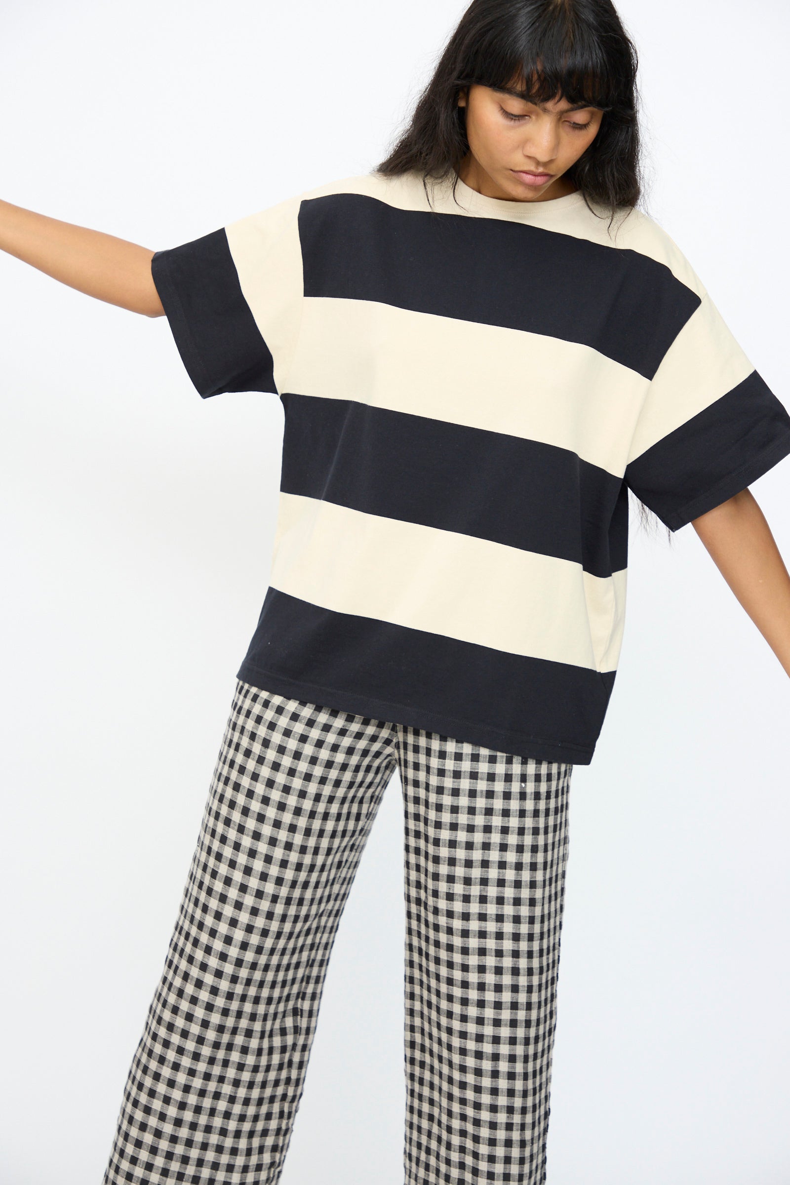 A person wears the Ichi Antiquités Cotton Stripe Pullover in Natural and Black, paired with black and white checkered pants, standing against a plain white background.
