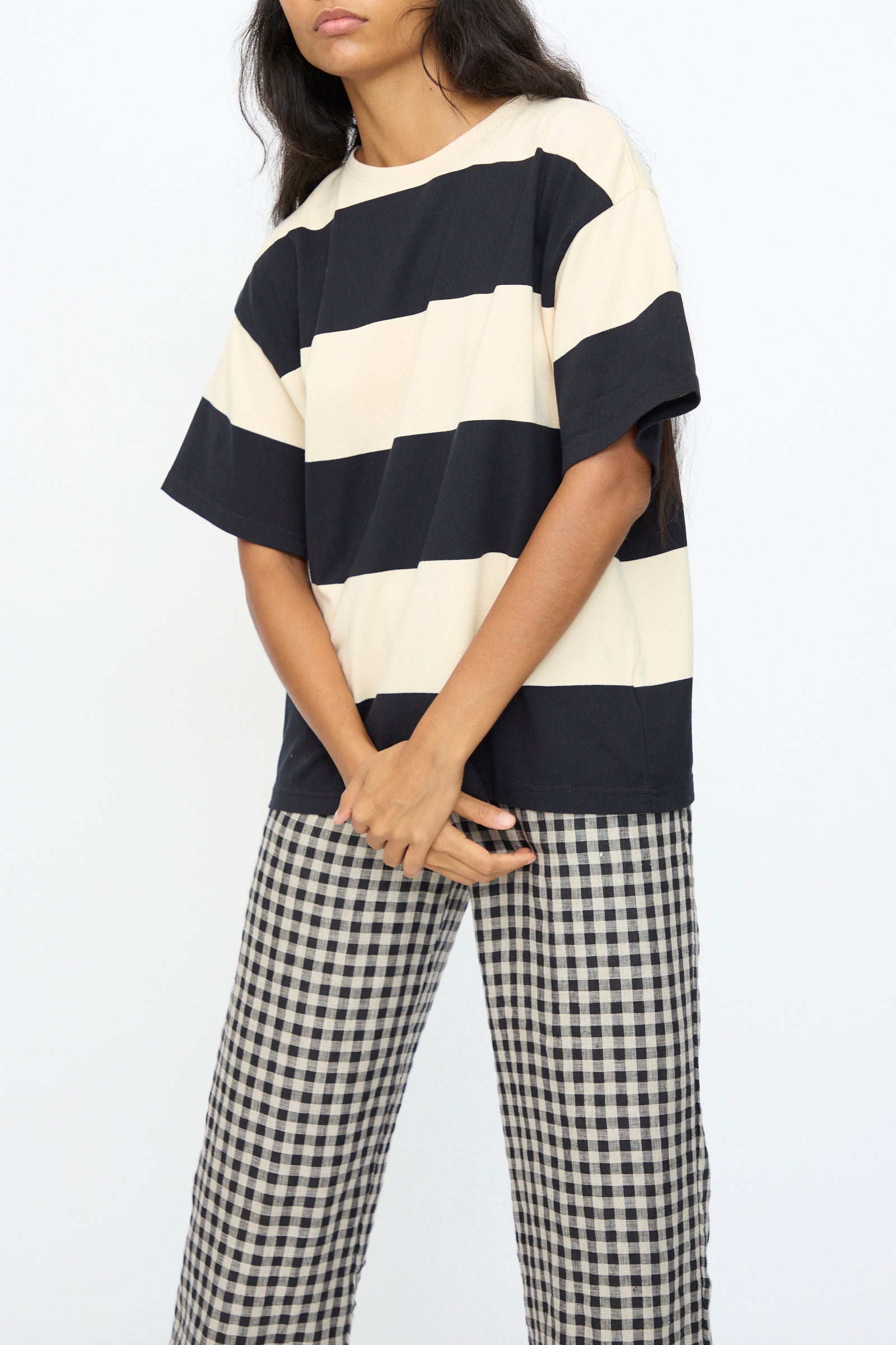 Person wearing the Ichi Antiquités Cotton Stripe Pullover in Natural and Black, paired with black-and-white checkered pants, stands against a plain white background. 