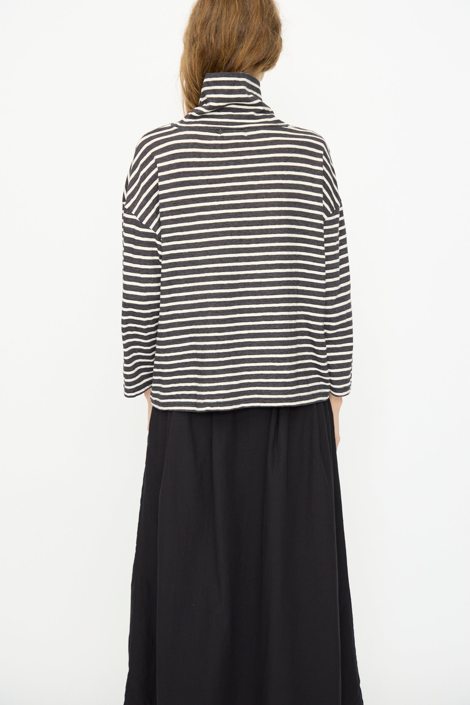 Person faces away from the camera, wearing the Ichi Antiquités Cotton Stripe Turtleneck in Charcoal with a black skirt, set against a plain white background.