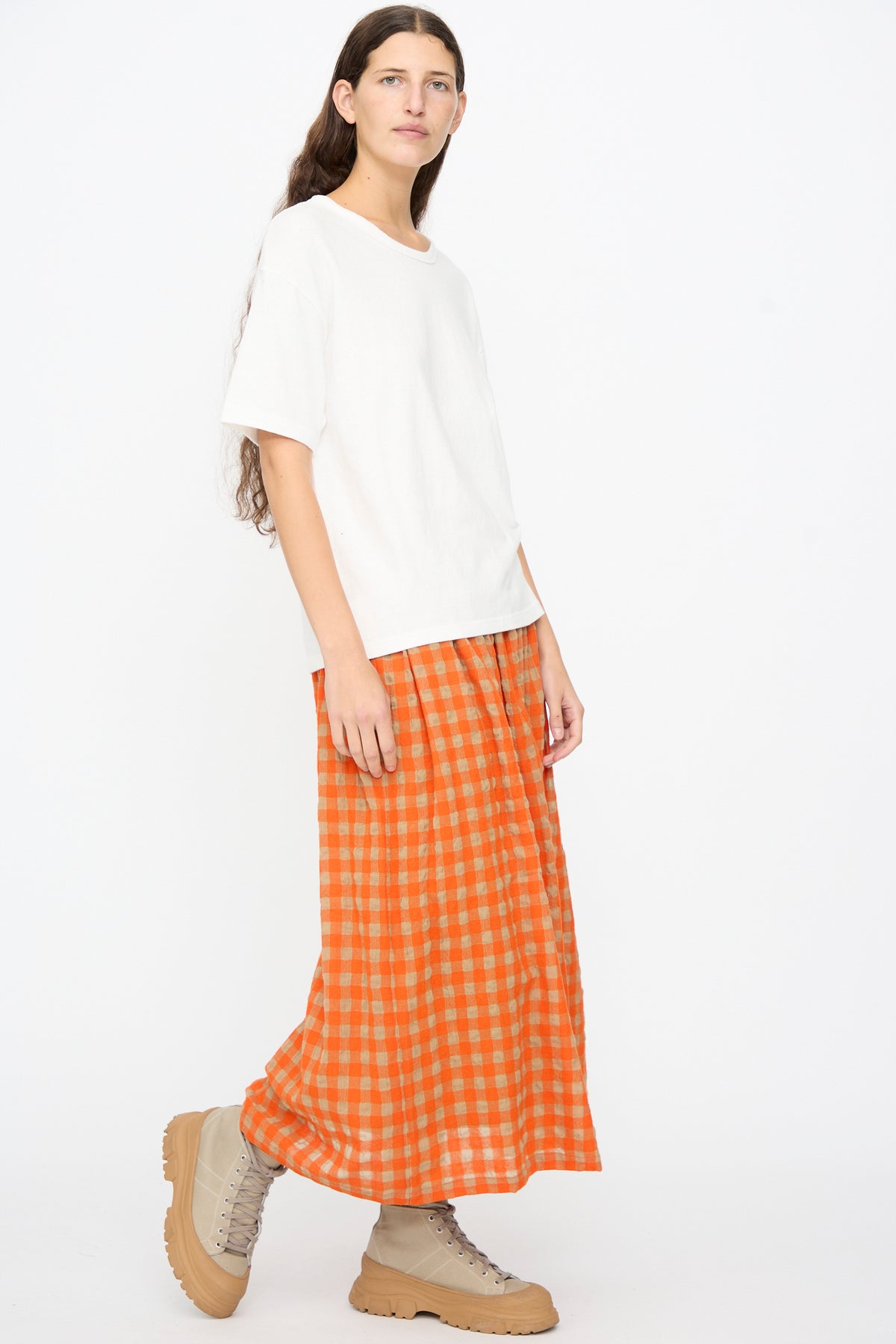 A person wearing a white Ichi Antiquités Cotton T-Shirt, a long orange and beige checkered skirt, and beige lace-up boots.