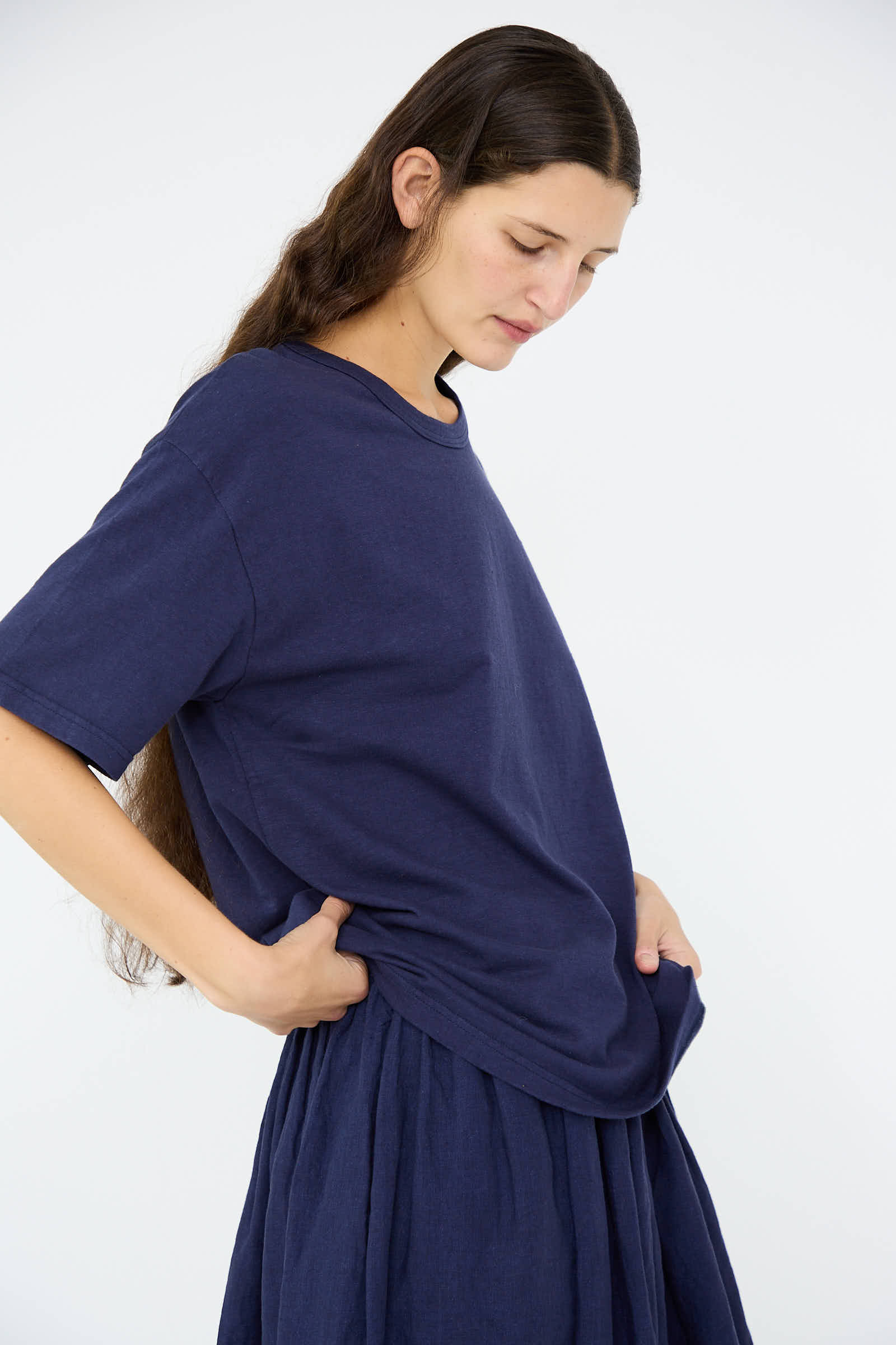 A person wearing the Cotton T-Shirt in Navy by Ichi Antiquités, crafted from medium weight cotton, stands with hands in pockets, gazing downward.