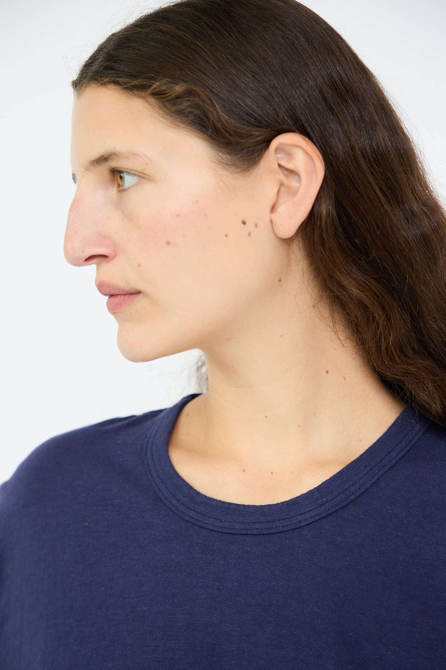 A person with long brown hair wearing an Ichi Antiquités Cotton T-Shirt in Navy, styled as a pullover tee with a boxy fit, is looking to the left against a plain background.