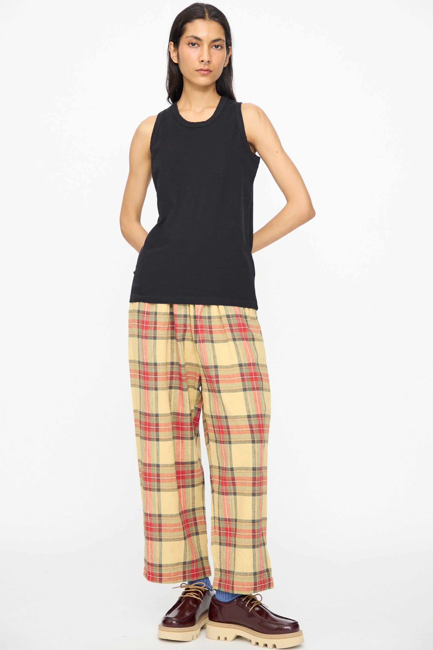 A person wearing the Ichi Antiquités Cotton Tank Top in Black, paired with yellow plaid wide-leg pants and brown platform shoes, stands against a plain white background.