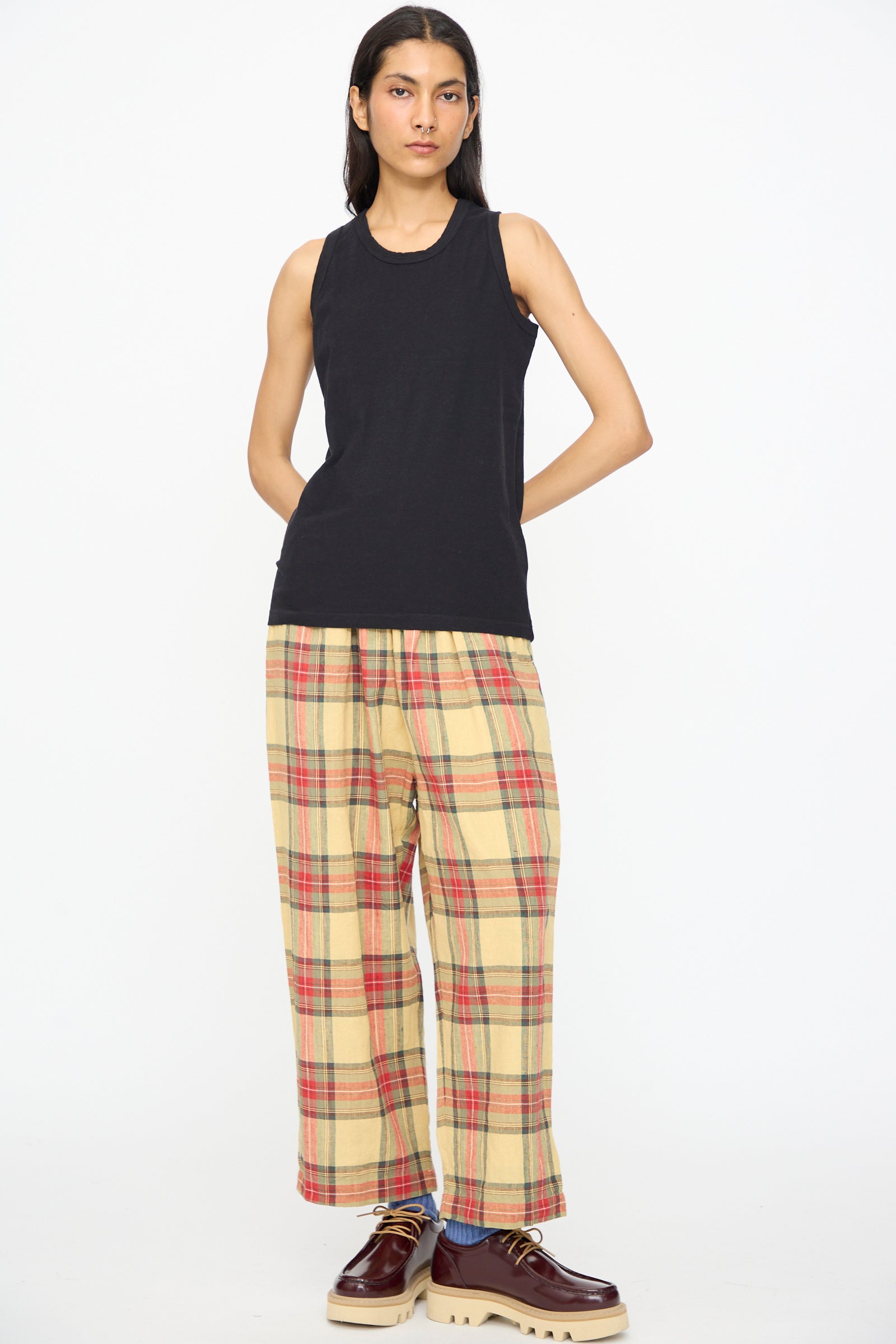 A person wearing the Ichi Antiquités Cotton Tank Top in Black, paired with yellow plaid wide-leg pants and brown platform shoes, stands against a plain white background.