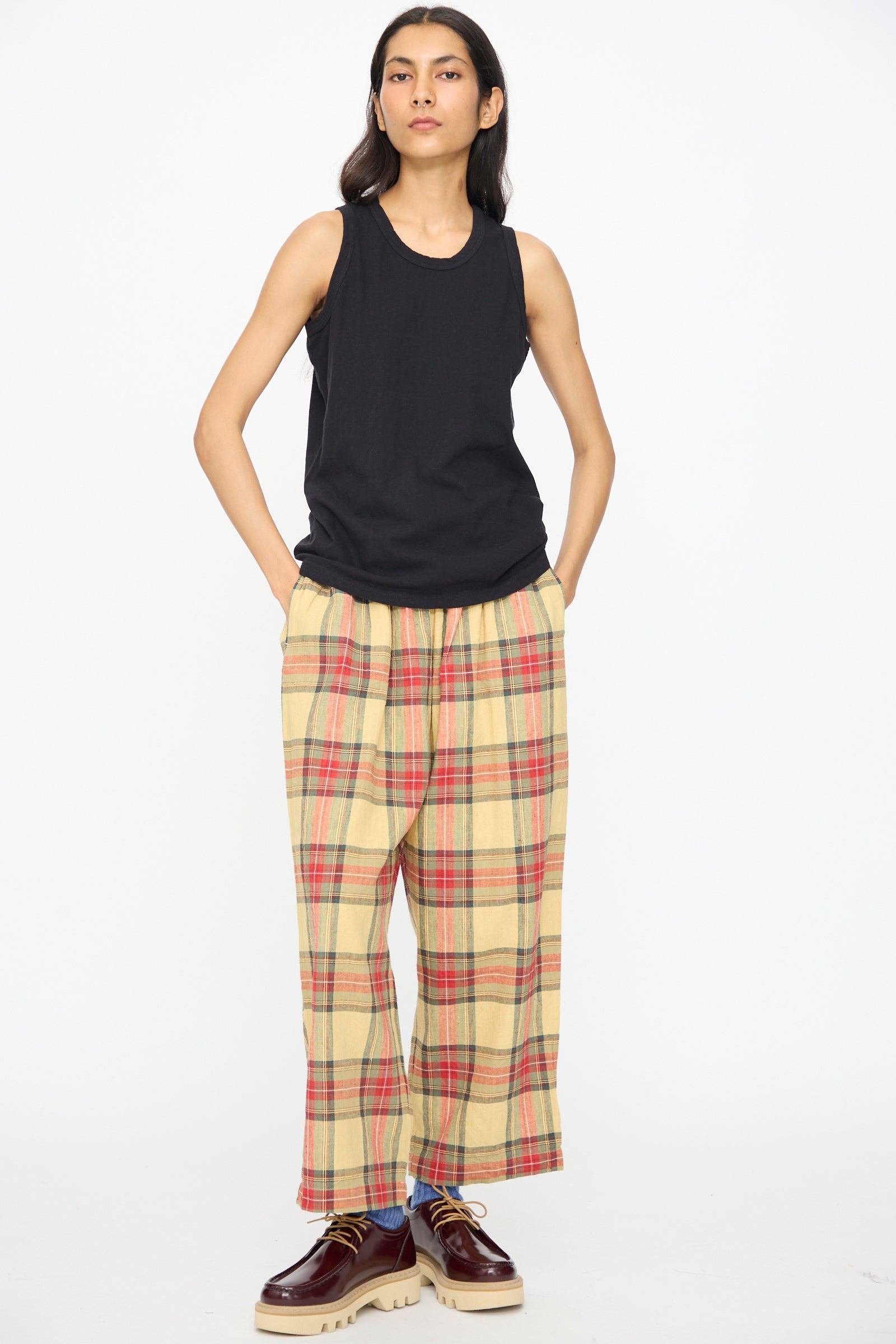 A person wears the Ichi Antiquités Cotton Tank Top in Black, a relaxed fit cotton piece made in Japan, paired with loose beige plaid pants, hands in pockets, against a plain white background.