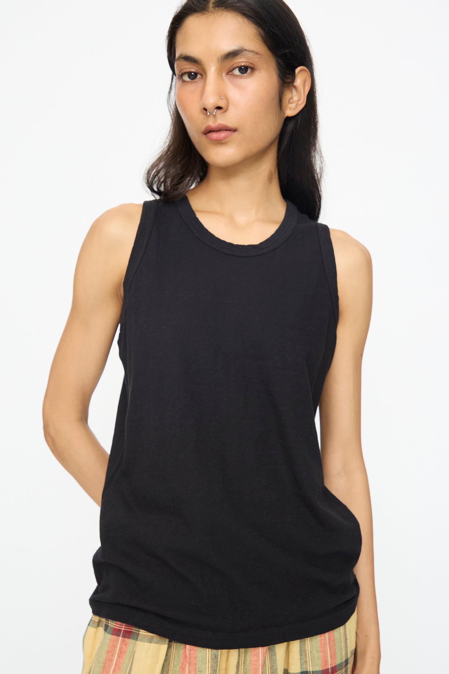 Person with long dark hair and a nose ring wears the Ichi Antiquités Cotton Tank Top in Black, styled with striped pants, against a plain white background. This relaxed-fit tank is crafted from cotton and made in Japan.