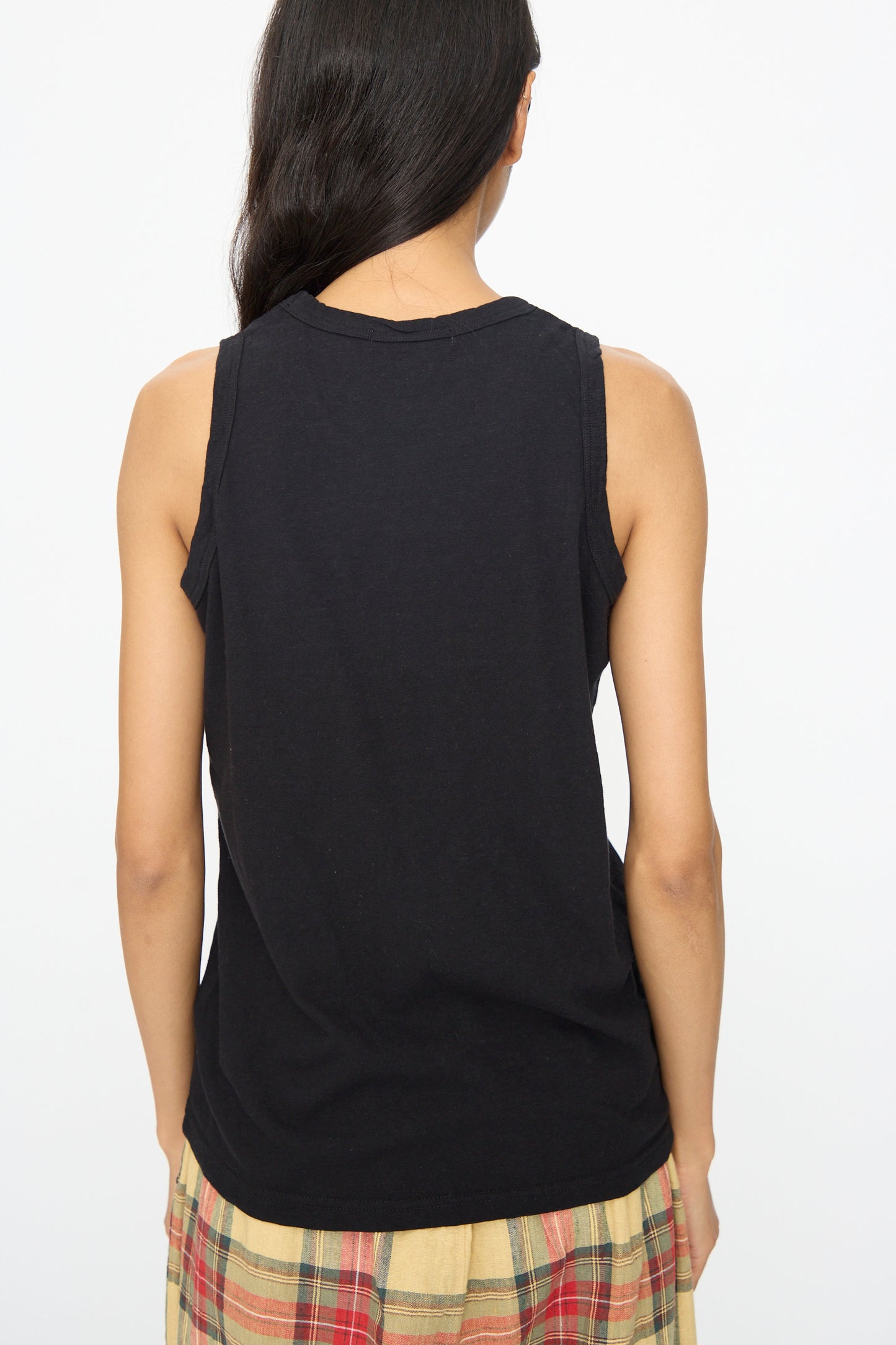 A person with long dark hair is shown from the back, wearing the Ichi Antiquités Cotton Tank Top in Black and a plaid skirt against a plain white background.
