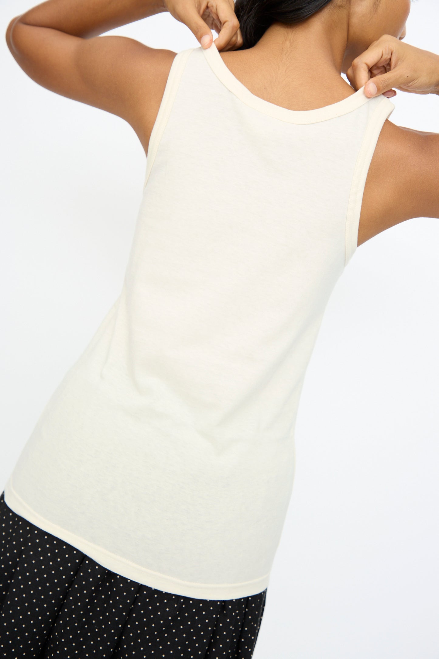 A model is shown from the back adjusting the neckline of the Ichi Antiquités Cotton Tank Top in Natural, paired with a black skirt featuring white polka dots.