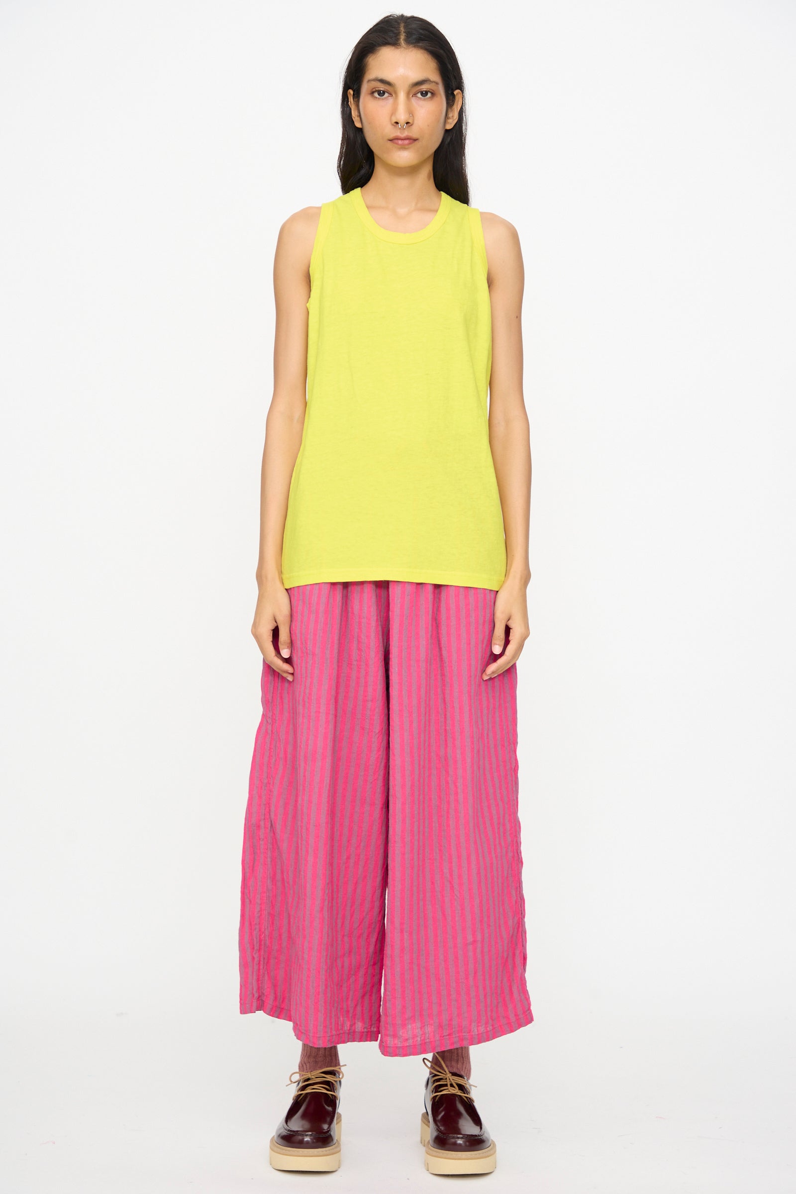 A person stands facing forward against a plain white background, wearing the Ichi Antiquités Cotton Tank Top in Yellow, wide-legged pink striped pants, and brown platform shoes.