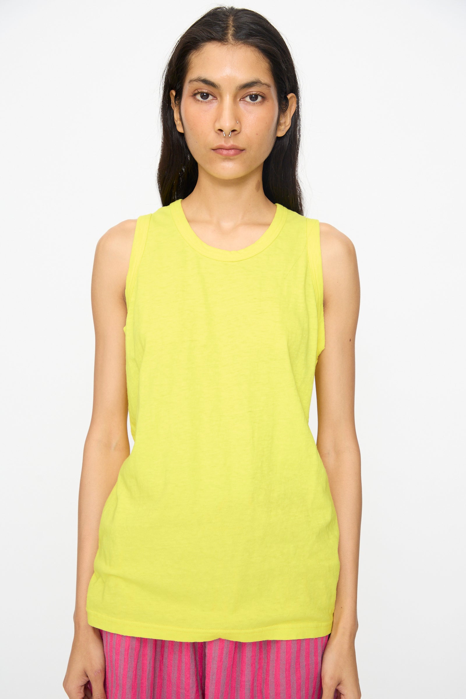A person wears the Ichi Antiquités Cotton Tank Top in Yellow, made in Japan, paired with pink striped pants, standing against a plain background and looking directly at the camera with a neutral expression.