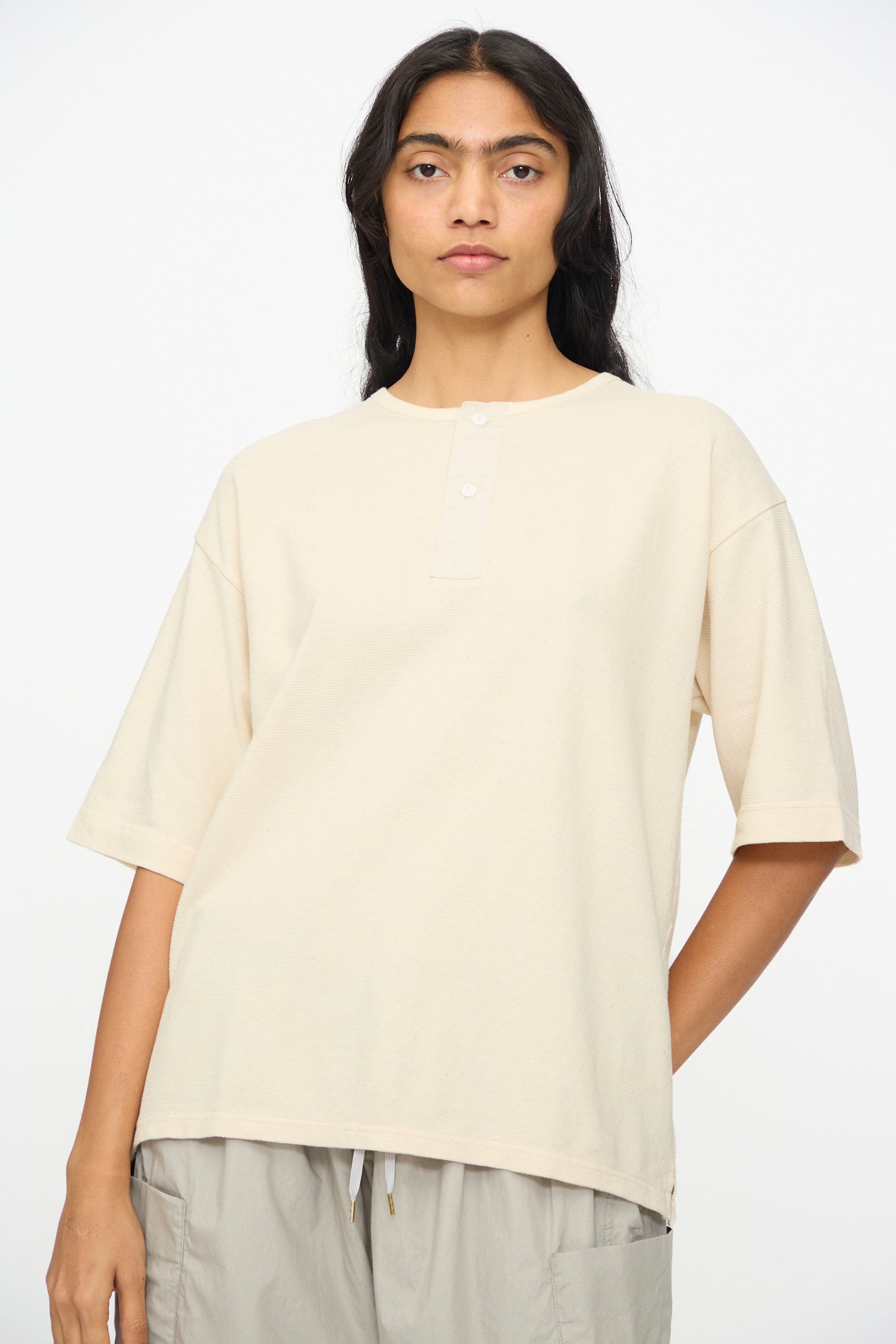 A person with long dark hair wears the Ichi Antiquités Cotton Thermal Henley Neck Pullover in Ivory, paired with light gray pants, standing against a plain white background.