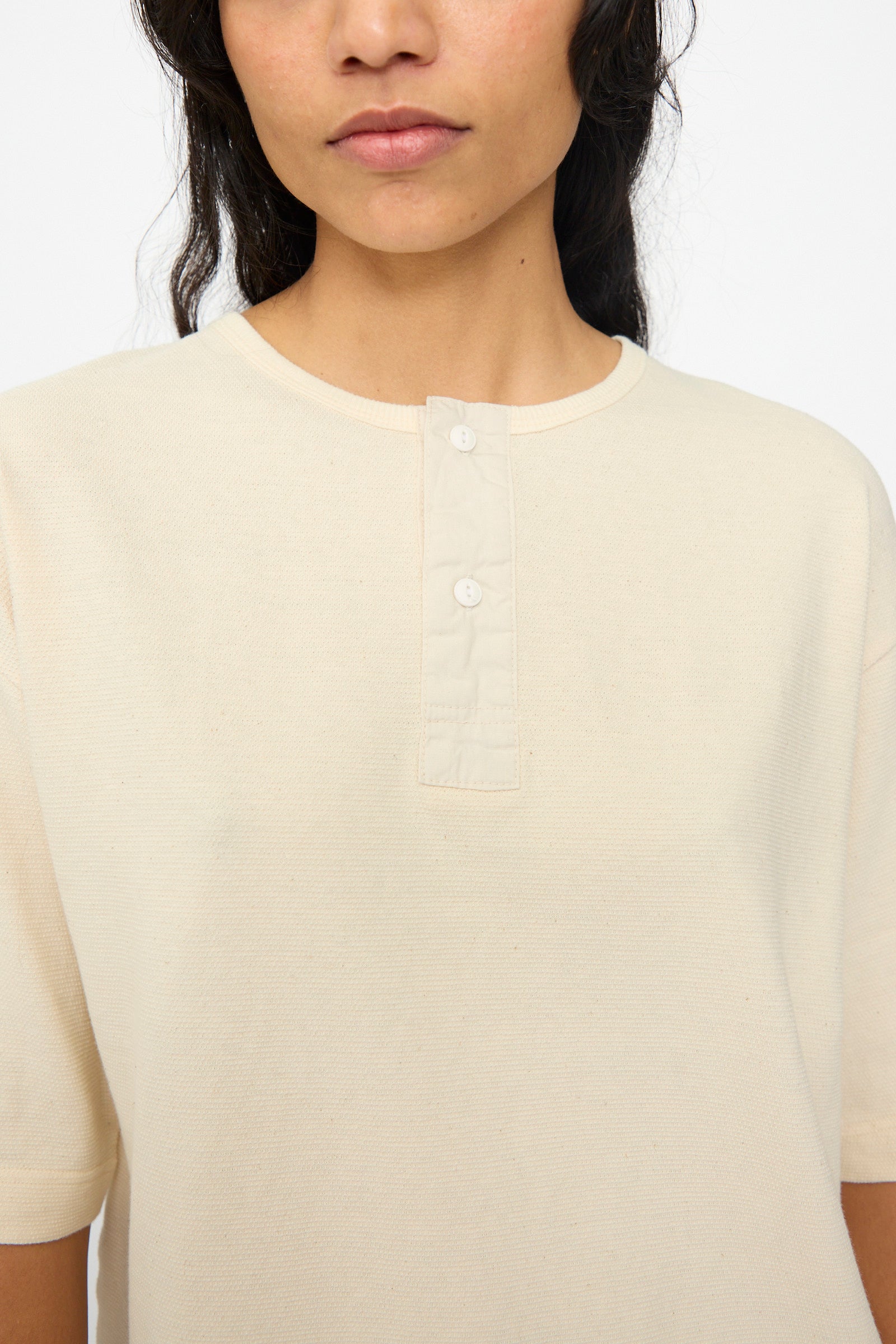 A person is shown from shoulders to mid-chest wearing the Ichi Antiquités Cotton Thermal Henley Neck Pullover in Ivory, featuring a relaxed fit, short sleeves, round neckline, and two-button placket.