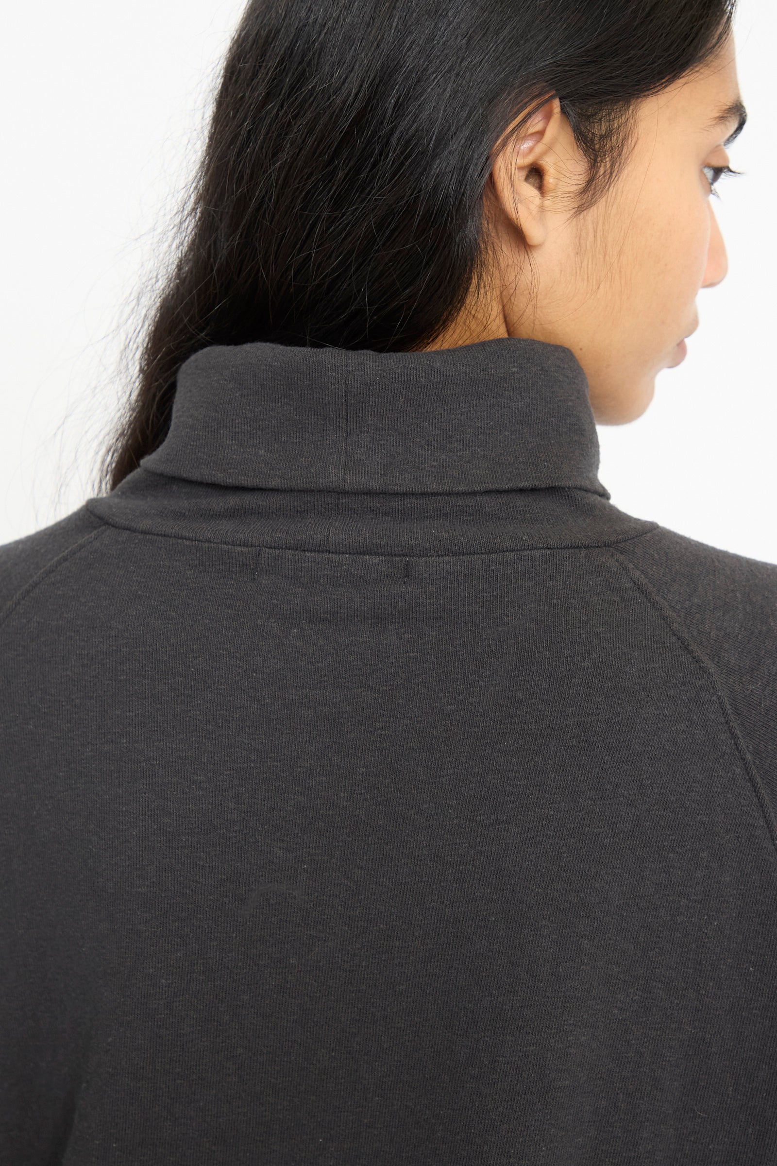 A close-up of a person with long dark hair from behind wearing the Ichi Antiquités Cotton Turtleneck in Black.