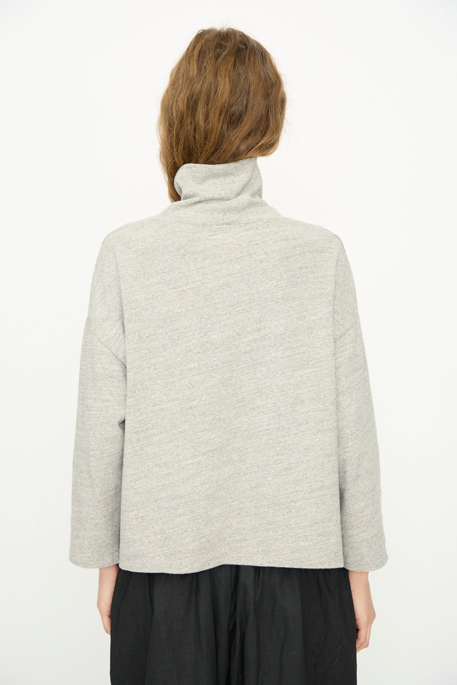 A person stands with their back to the camera, wearing the Ichi Antiquités Cotton Turtleneck in Gray paired with a black skirt, set against a plain white background.