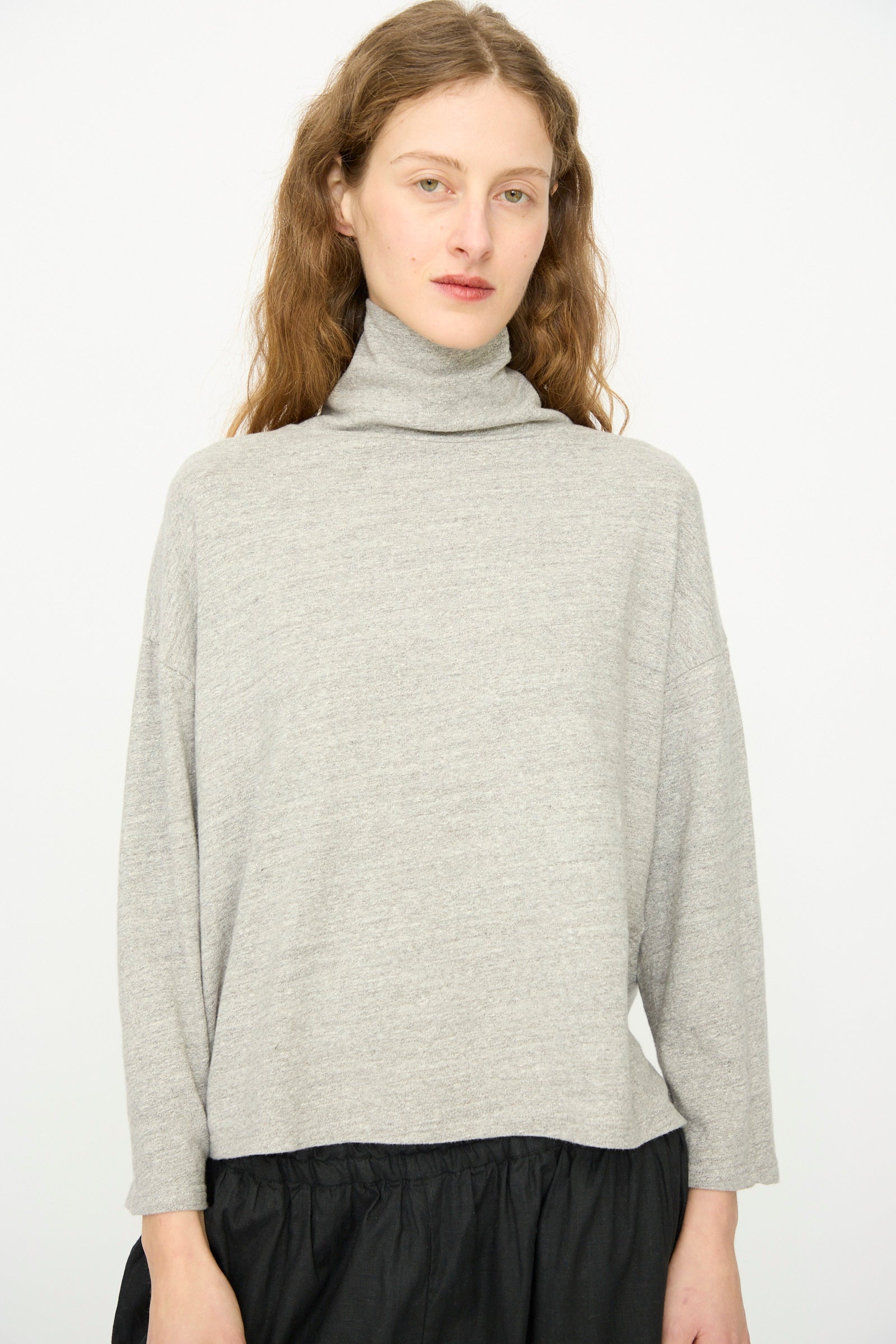 A person with long brown hair wears the Cotton Turtleneck in Gray by Ichi Antiquités and a black skirt, standing against a plain white background.