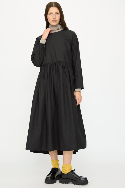 A woman poses against a white background in the Ichi Antiquités Cotton Typewriter Dress in Black, styled with a taupe turtleneck, yellow socks, and black platform shoes.