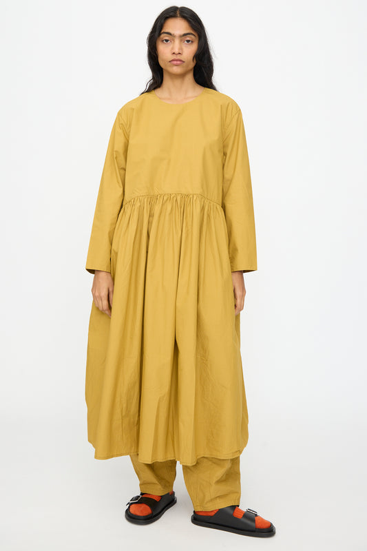 A model wears the Ichi Antiquités Cotton Typewriter Dress in Mustard, paired with matching wide pants and black-and-orange sandals, standing against a plain white background.