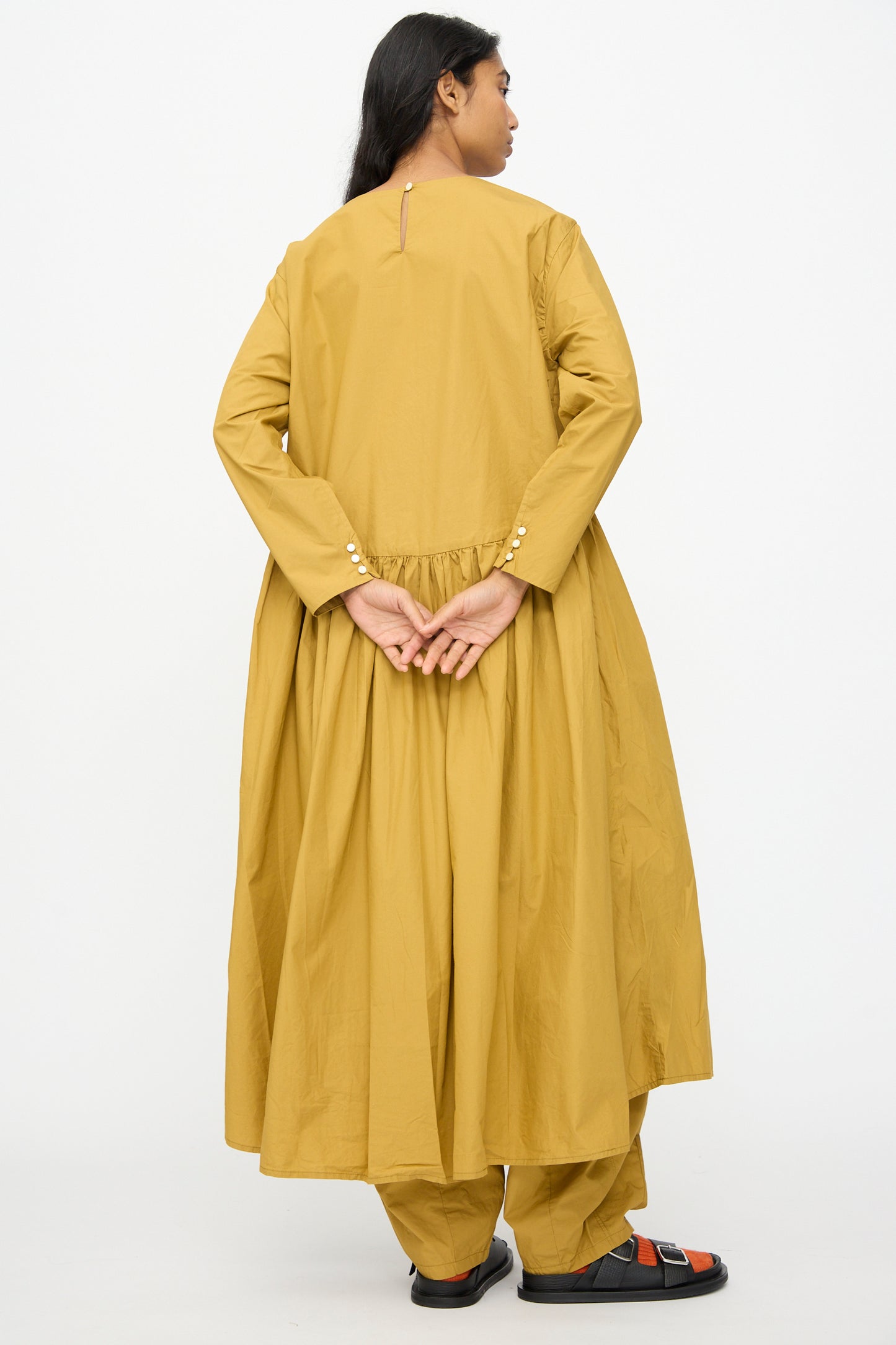 Model stands with hands clasped behind back, wearing the Ichi Antiquités Cotton Typewriter Dress in Mustard, photographed from behind against a plain white background.