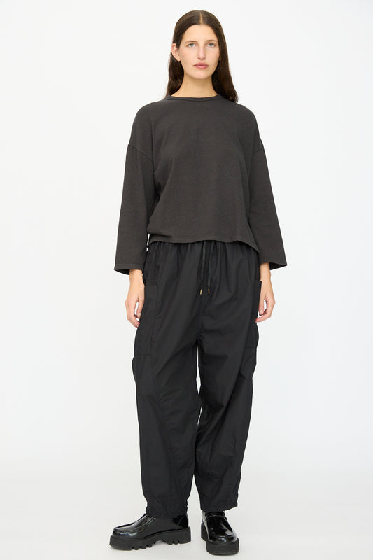 A woman stands facing forward in a loose dark long-sleeve top, Ichi Antiquités Cotton Typewriter Pants in Black made in Japan, and black chunky shoes against a plain white background.