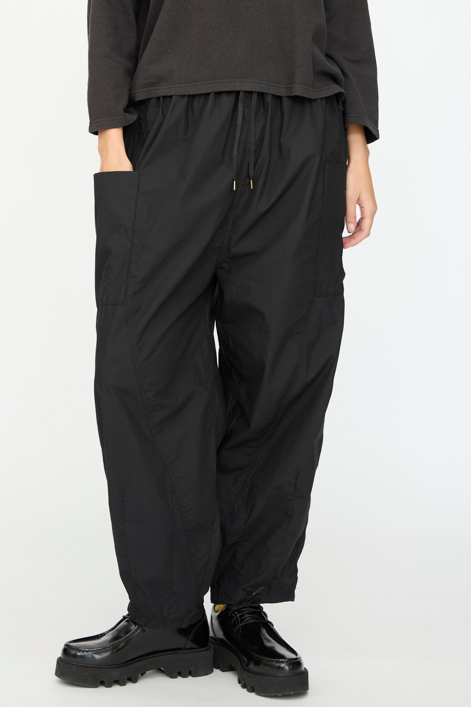 A person wears Ichi Antiquités’ Cotton Typewriter Pants in Black—loose fit with a drawstring waist and large side pockets—paired with black platform shoes, standing against a plain light background. Made in Japan.