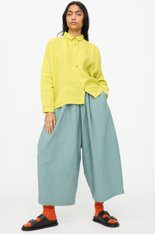 A person wears a loose yellow button-up shirt, Ichi Antiquités Cotton Typewriter Pants in Ice Blue, orange socks, and black sandals, standing against a plain white background.