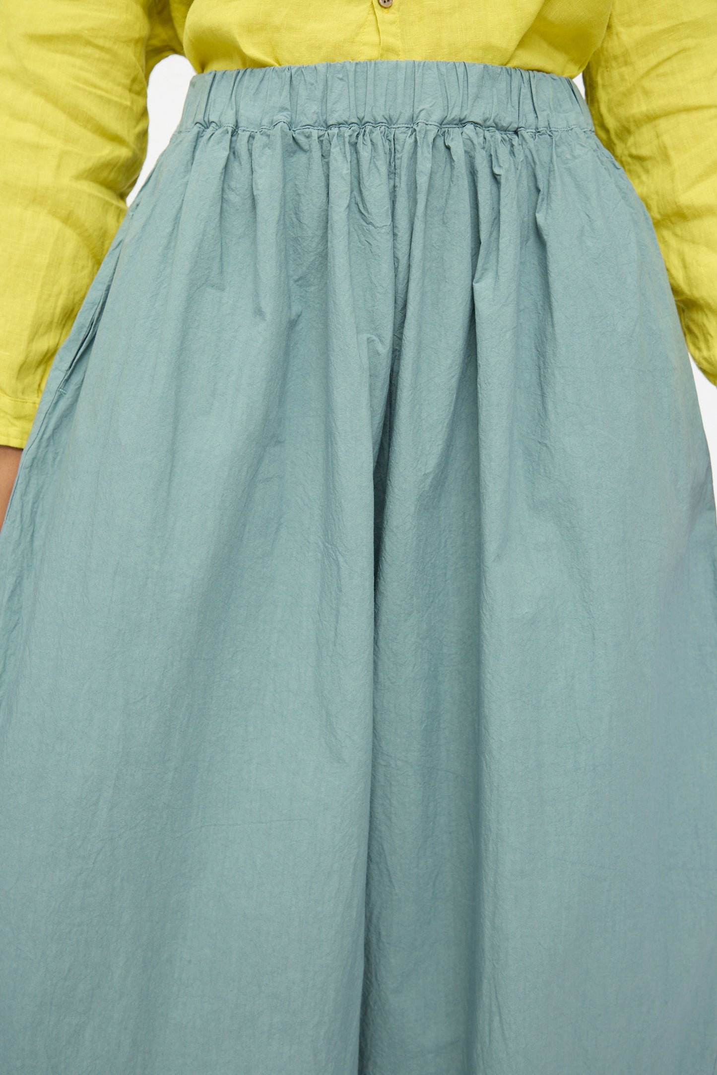 A person wearing a yellow long-sleeve shirt tucked into a high-waisted light blue skirt, layered with wide cropped Cotton Typewriter Pants in Ice Blue by Ichi Antiquités for a stylish Japanese-inspired look.