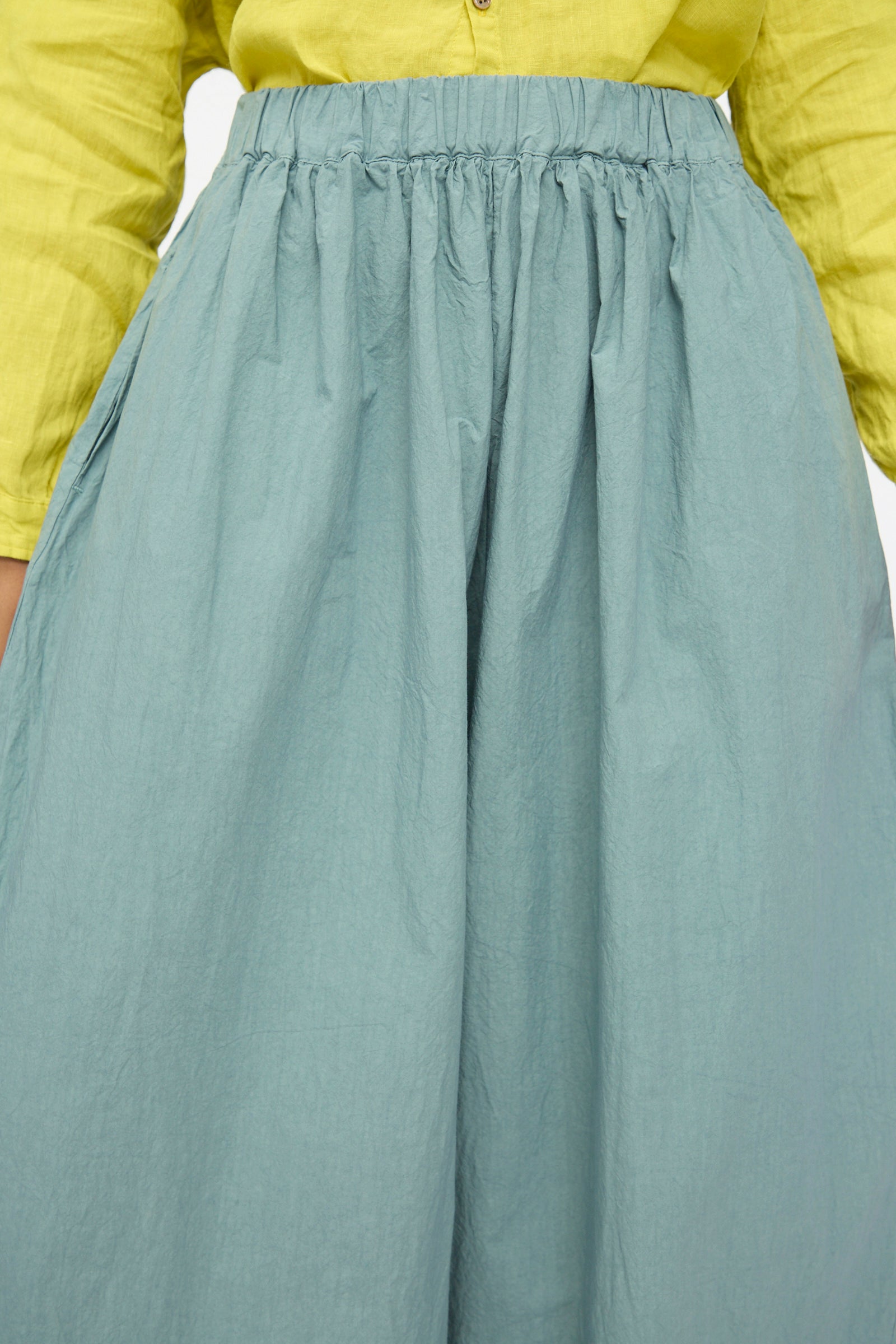 A person wearing a yellow long-sleeve shirt tucked into a high-waisted light blue skirt, layered with wide cropped Cotton Typewriter Pants in Ice Blue by Ichi Antiquités for a stylish Japanese-inspired look.