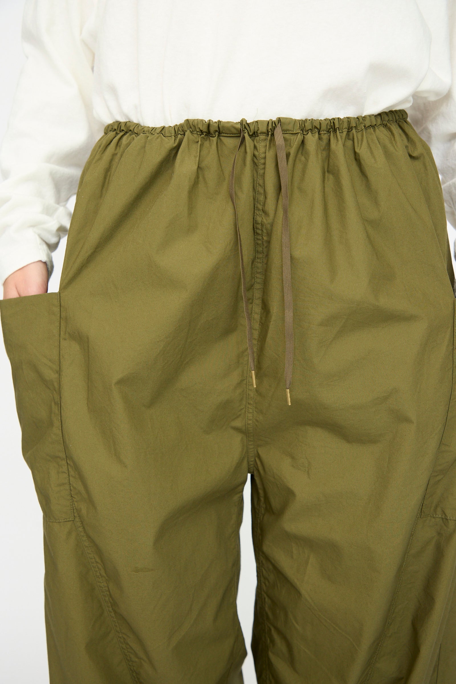 A person wears Ichi Antiquités Cotton Typewriter Pants in khaki—loose, with large side pockets—paired with a white long-sleeve shirt. Made in Japan, these pants blend comfort, utility, and style.