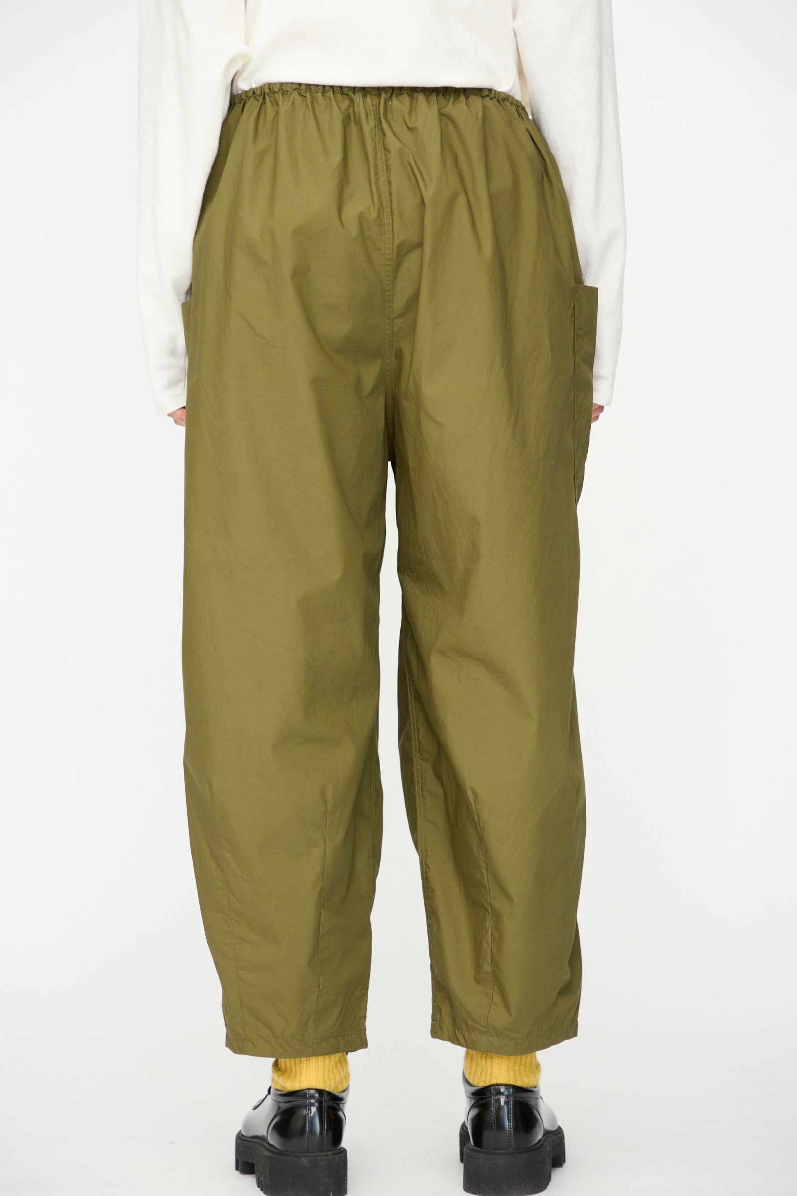 Person wearing Ichi Antiquités Cotton Typewriter Pants in khaki, yellow socks, black shoes, and a white long-sleeve top, photographed from the back against a plain background.
