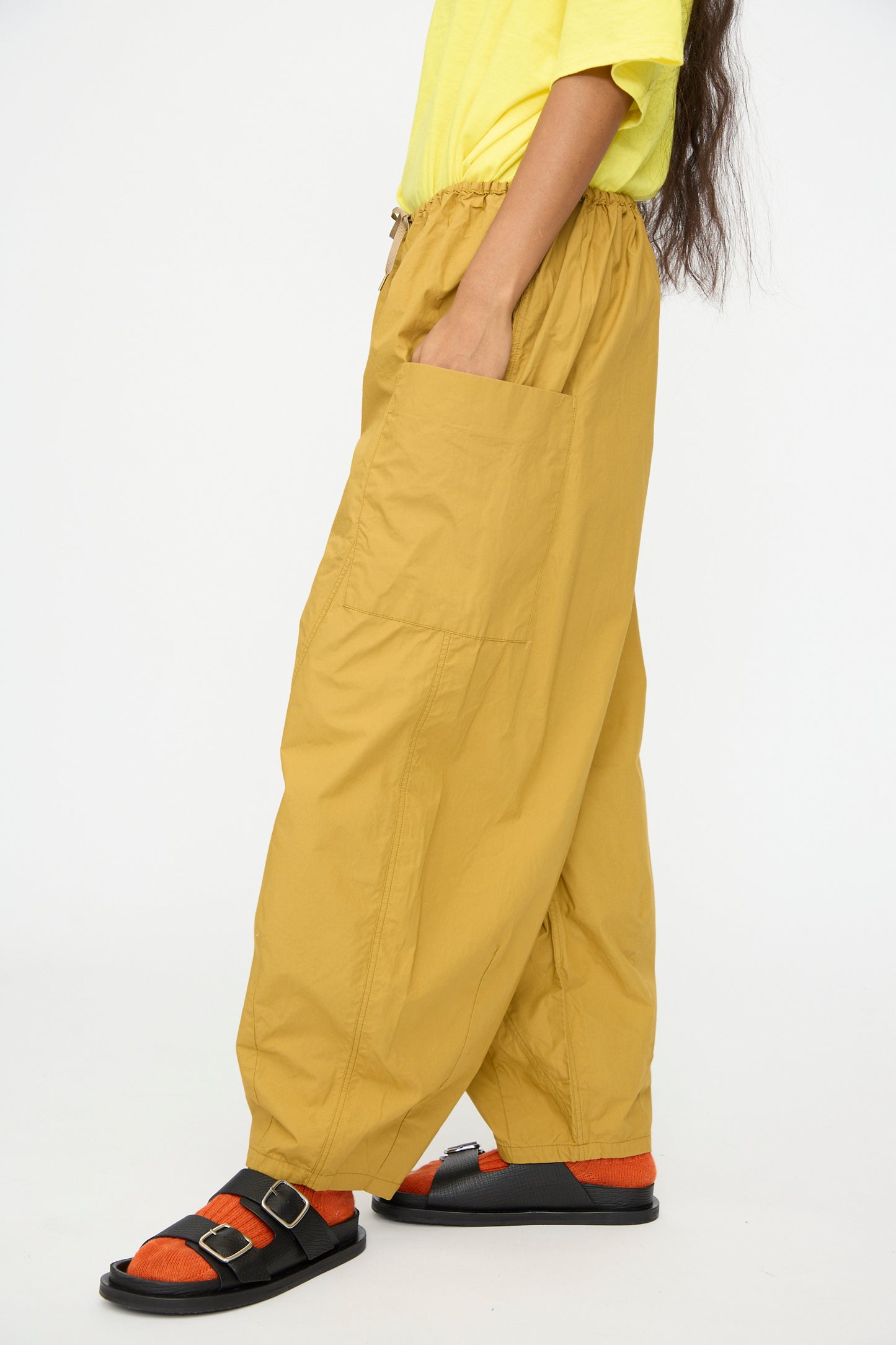 Someone wearing Ichi Antiquités Cotton Typewriter Pants in Mustard, paired with a light yellow shirt, orange socks, and black sandals, stands against a plain white background.
