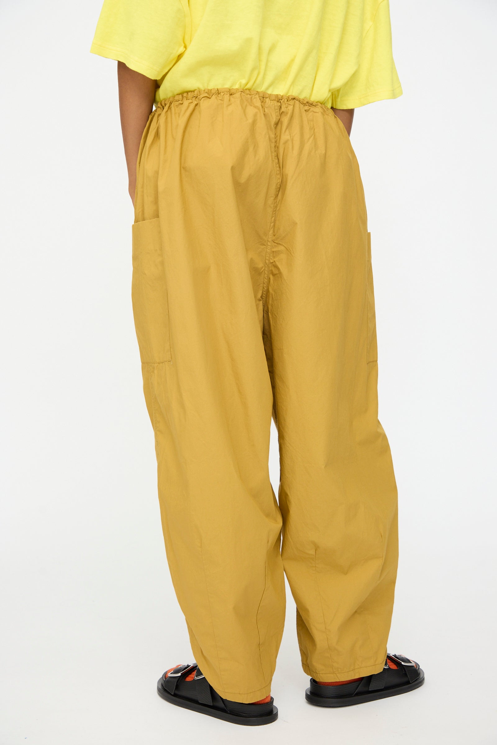 A person shown from the back against a plain white background wears Ichi Antiquités Cotton Typewriter Pants in Mustard, styled with a yellow T-shirt and black sandals.