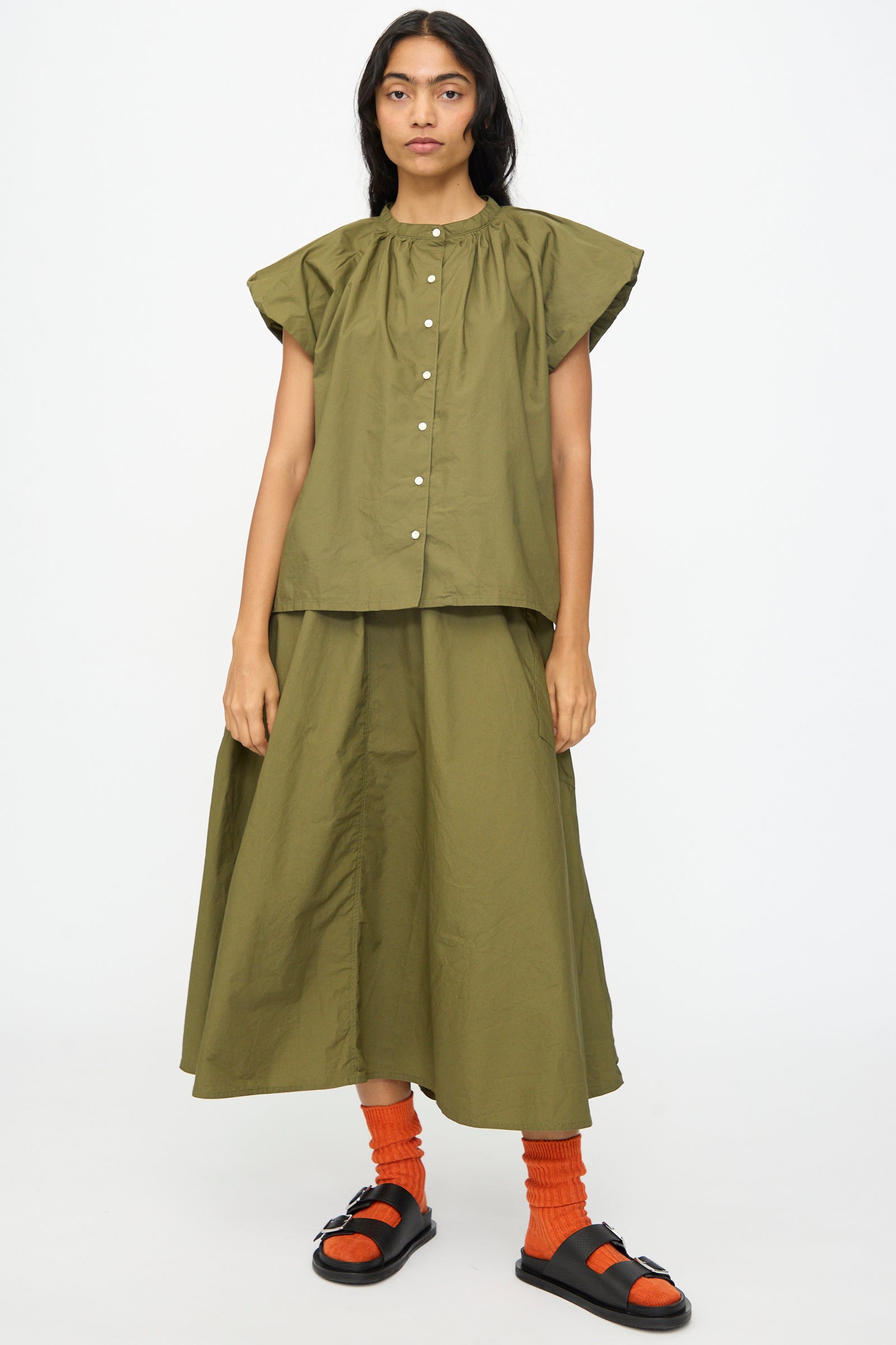 A person faces forward wearing the Ichi Antiquités Cotton Typewriter Shirt in Khaki with a matching skirt, orange socks, and black sandals, against a plain white background.