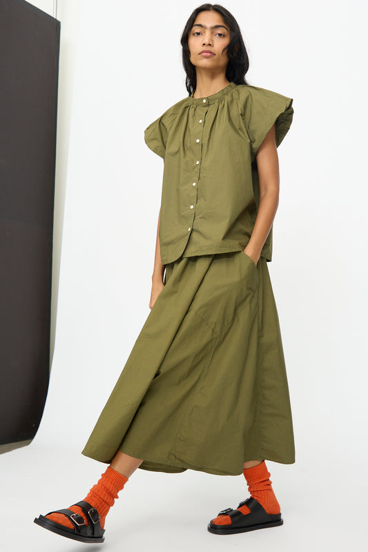 A person wears the Ichi Antiquités Cotton Typewriter Shirt in Khaki with a matching skirt, orange socks, and black sandals, standing against a plain background.