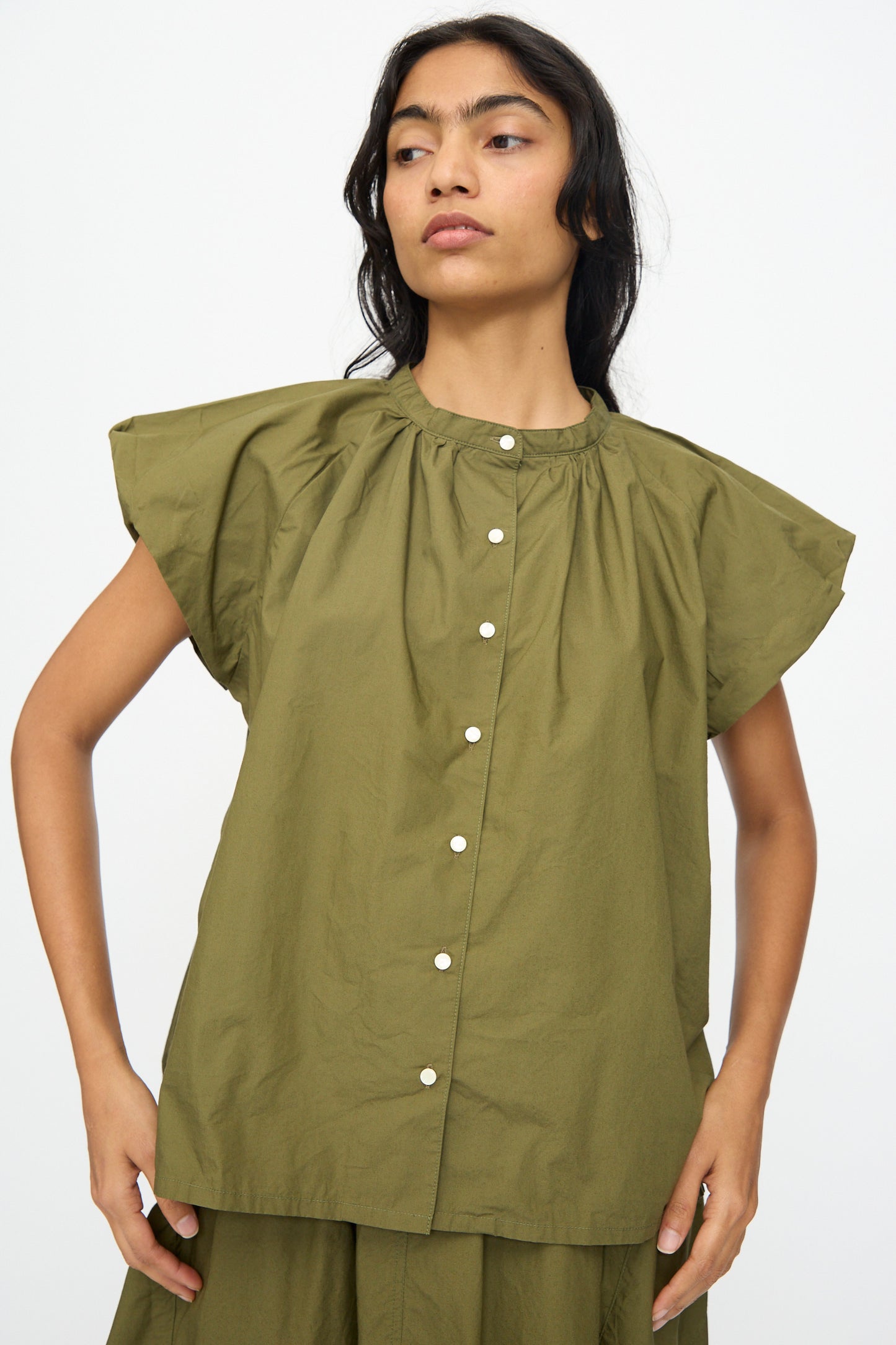 A woman wears the Ichi Antiquités Cotton Typewriter Shirt in khaki, featuring short sleeves, a gathered neckline, front buttons, and a loose fit, standing against a plain white background.