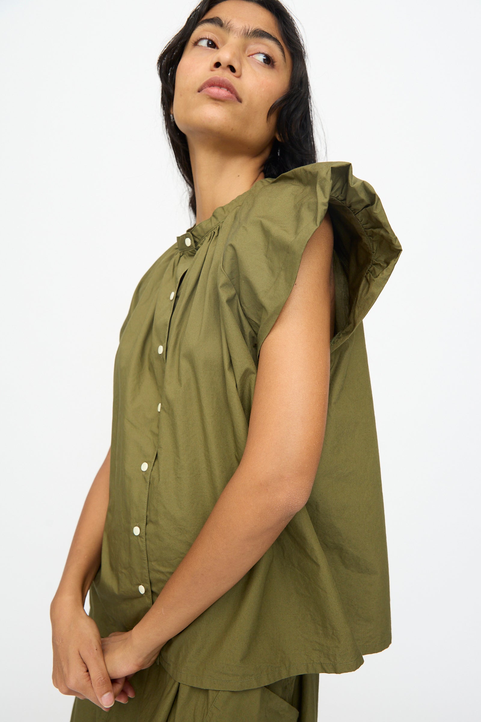 Model wearing the Ichi Antiquités Cotton Typewriter Shirt in khaki, a sleeveless cotton top with ruffled shoulders and front buttons, gazes upward against a plain white background.