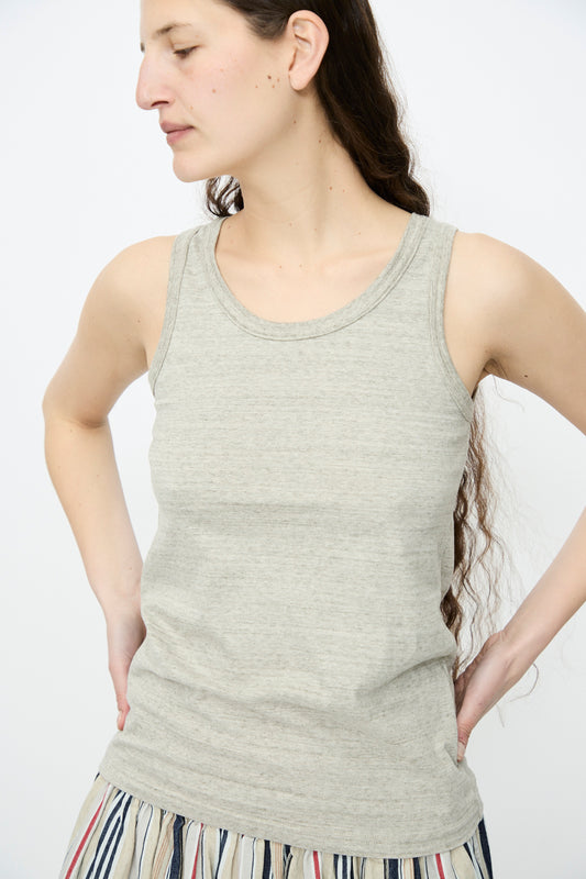 A person with long hair is wearing an Ichi Antiquités Cotton Undyed Tank Top in Gray and a striped skirt, standing with hands on hips against a plain background.