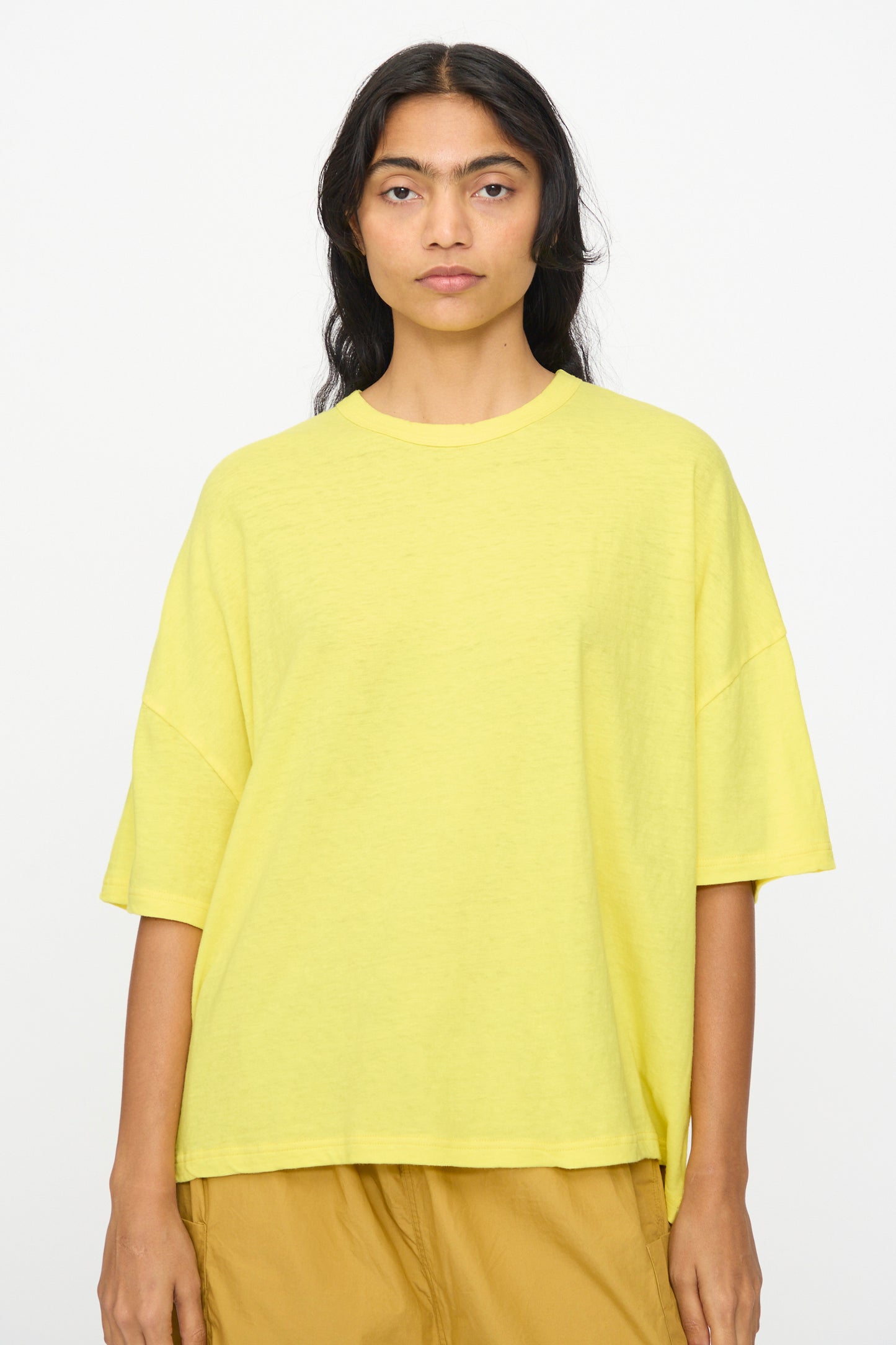 A person with long dark hair wears the Ichi Antiquités Cotton Wide Tee in Yellow and tan pants, standing against a plain white background.