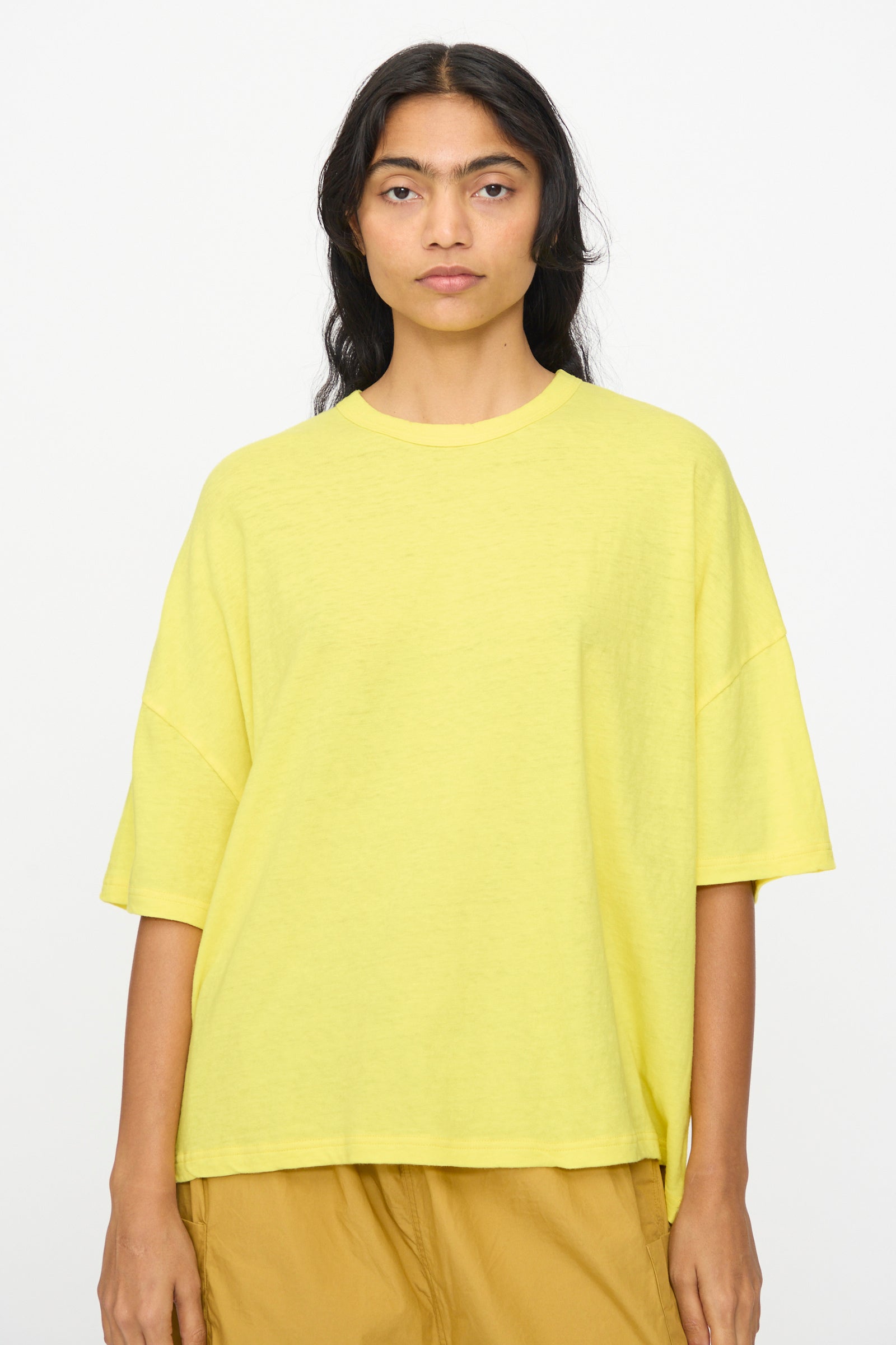 A person with long dark hair wears the Ichi Antiquités Cotton Wide Tee in Yellow and tan pants, standing against a plain white background.