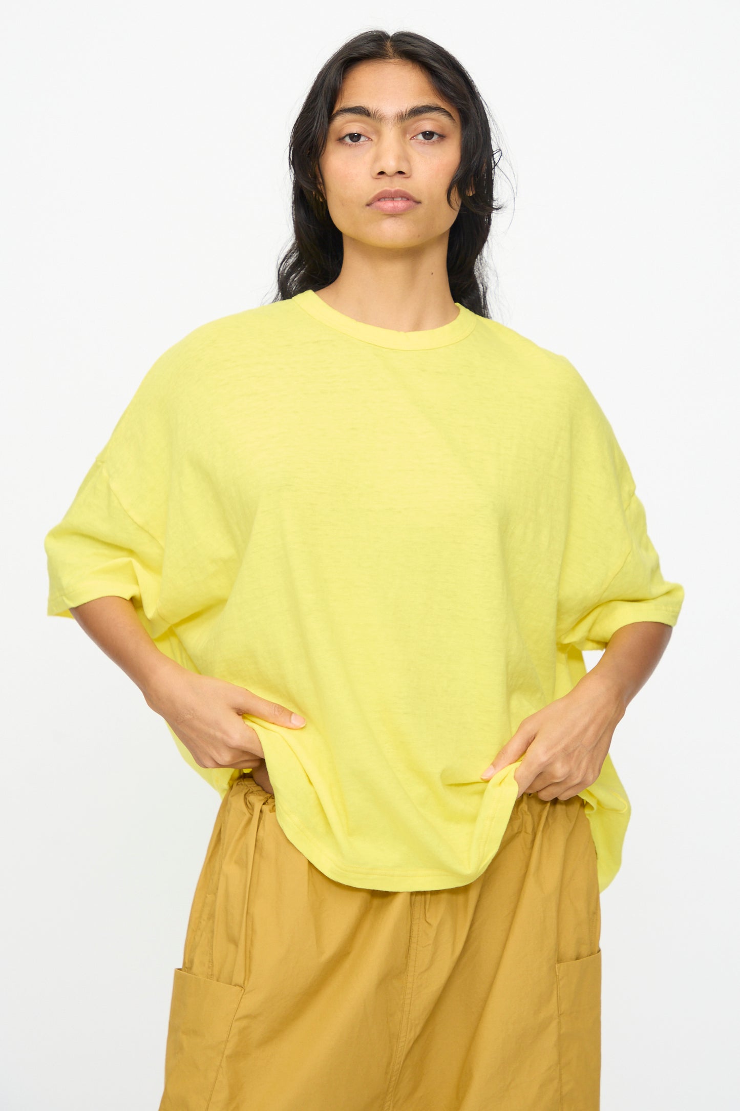 A person with long dark hair wears the Ichi Antiquités Cotton Wide Tee in Yellow and light brown pants, standing against a plain white background.