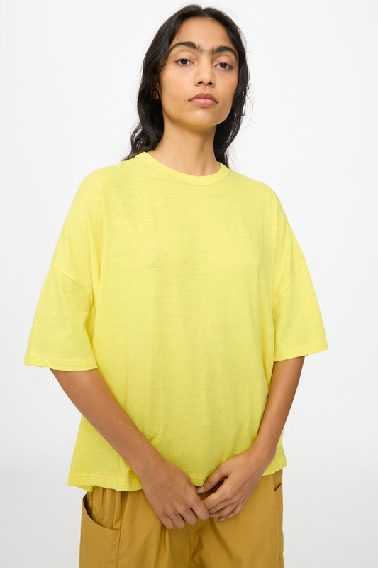 A person stands against a plain background wearing the Ichi Antiquités Cotton Wide Tee in Yellow and mustard-colored pants, with hands resting in front.