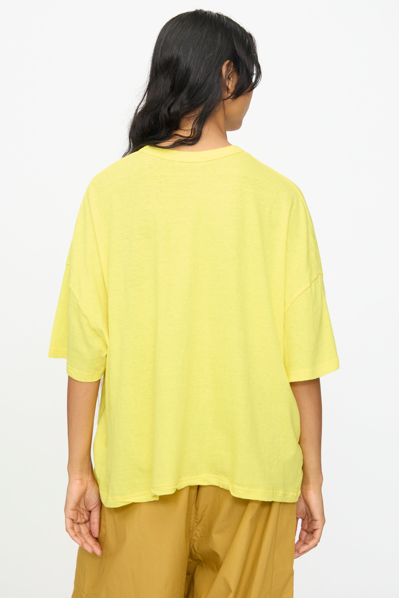 A person stands with their back to the camera, wearing the Ichi Antiquités Cotton Wide Tee in Yellow and brown pants against a plain white background.
