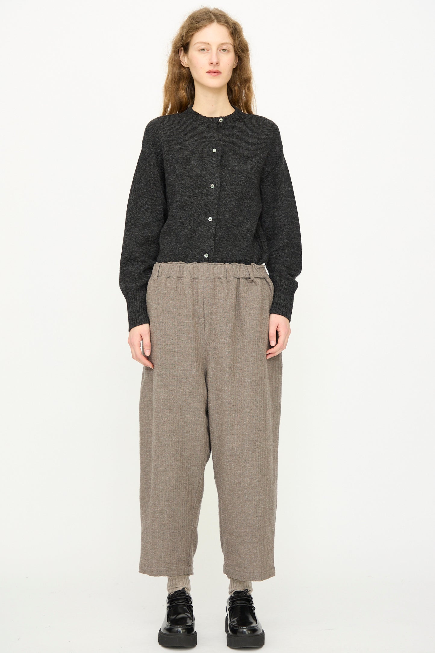 A person faces forward against a white background wearing Ichi Antiquités' Cotton Wool Sucker Pant in Mocha, styled with a dark buttoned cardigan and black shoes.
