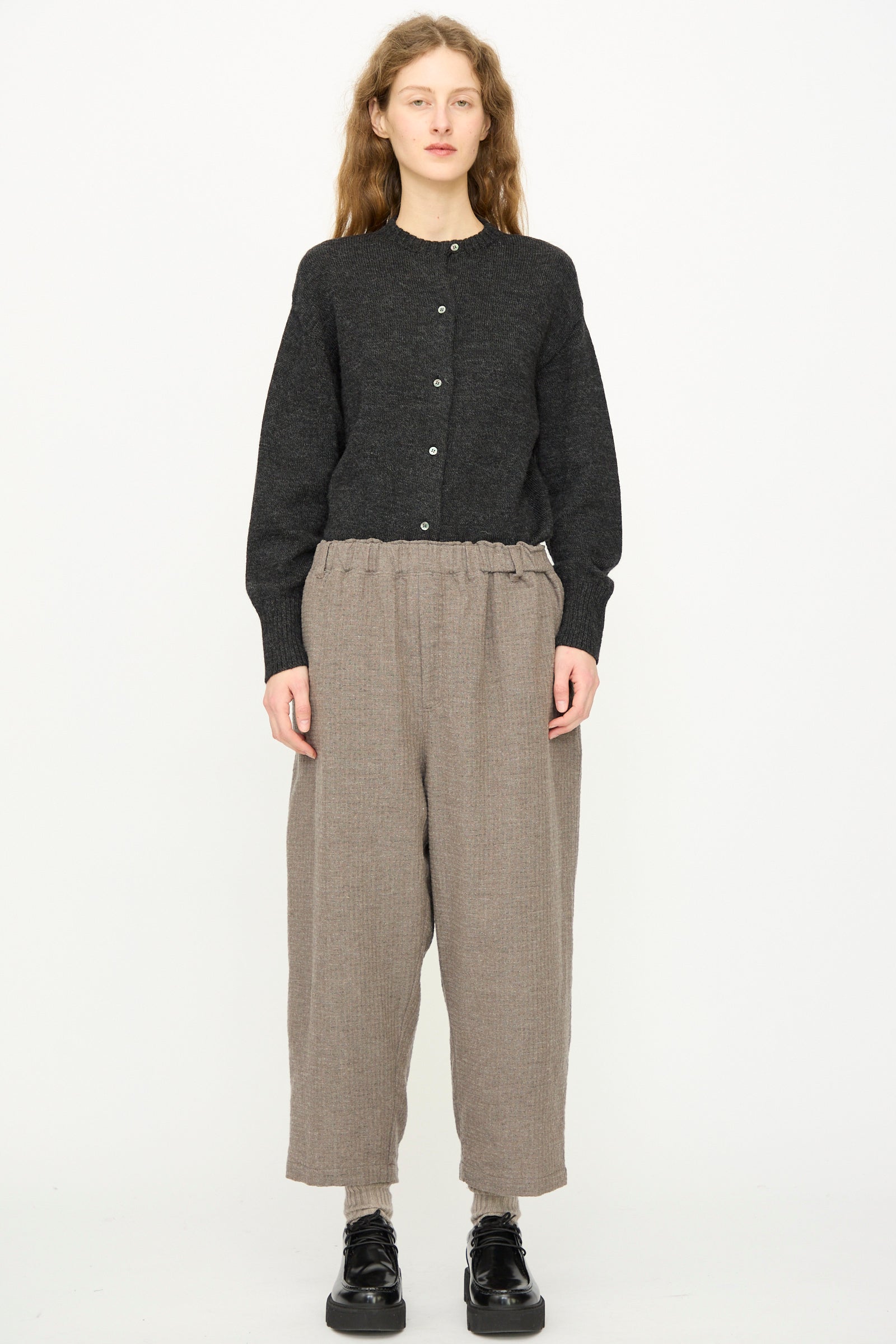 A person faces forward against a white background wearing Ichi Antiquités' Cotton Wool Sucker Pant in Mocha, styled with a dark buttoned cardigan and black shoes.