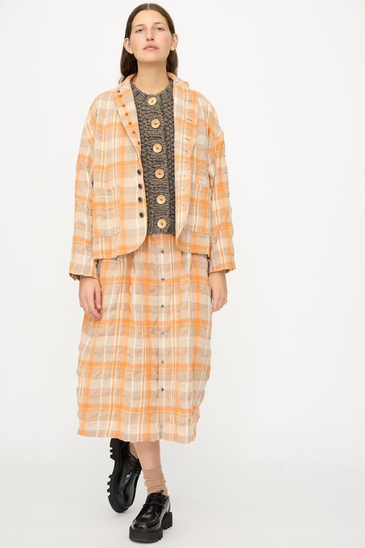 A person wears the Ichi Antiquités Cotton Wool Tartan Check Jacket in Orange, styled with a dark textured top, matching skirt, and black chunky shoes, standing against a plain white background.