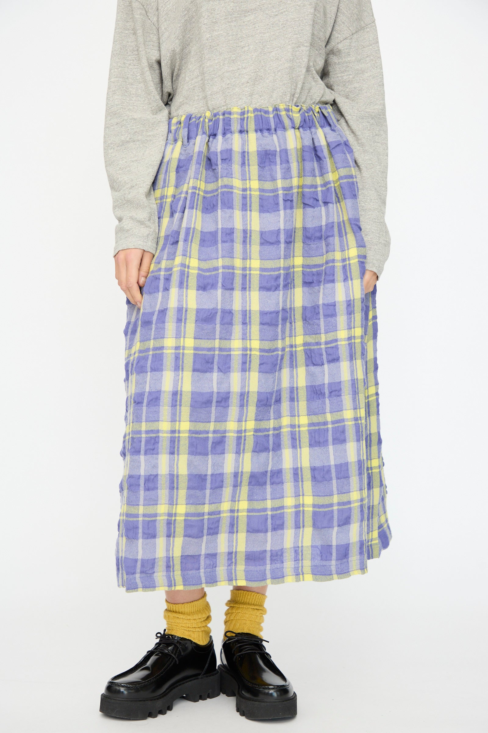 Someone stands against a plain background wearing a gray long-sleeve top, yellow socks, black shoes, and the Ichi Antiquités Cotton Wool Tartan Check Skirt in Blue, featuring an elastic waist and blue-and-yellow plaid pattern.